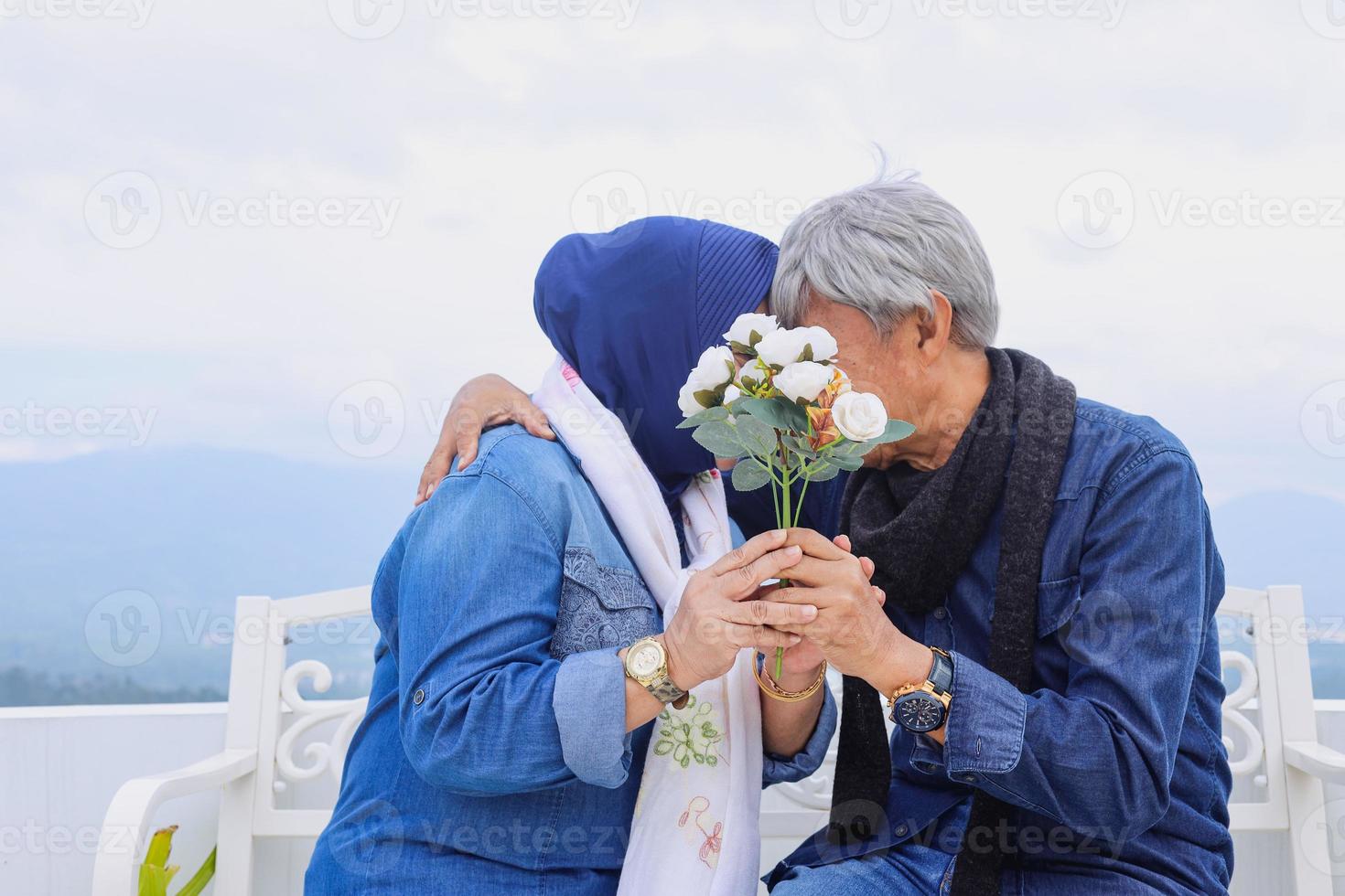 Romantic elderly couple kissing and covering their face together with white flower. photo