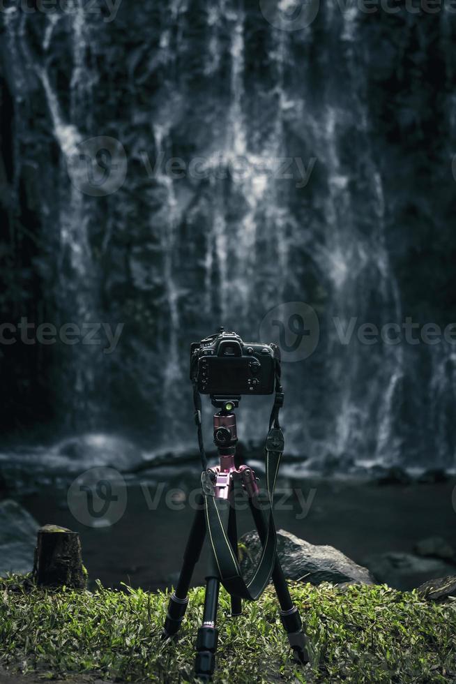 Modern camera is set on tripod for landscape photography in front of waterfall. photo