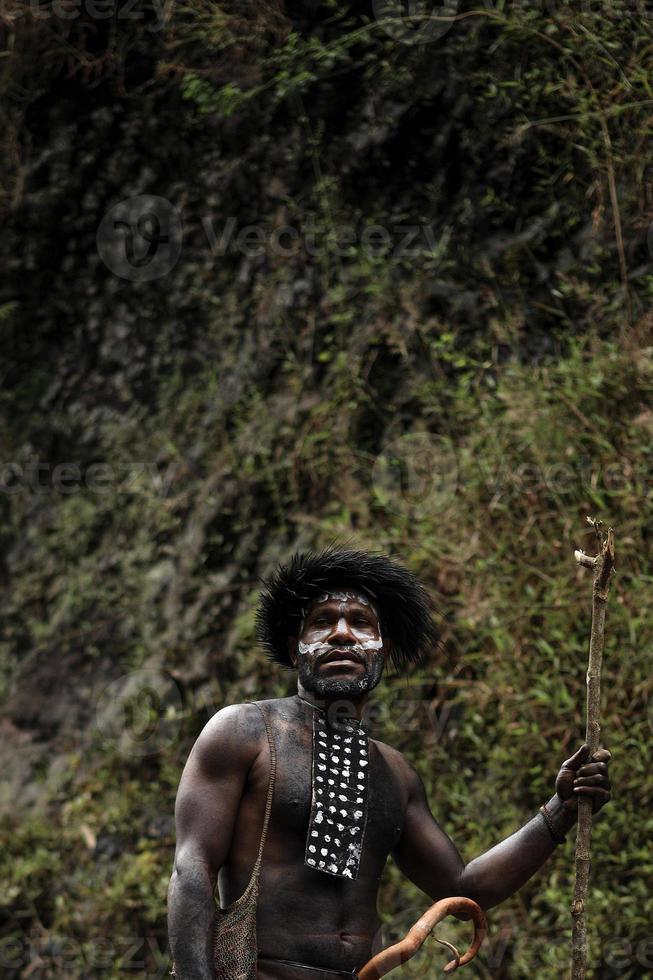 Portrait of Dani Tribe man wearing koteka, traditional clothes of Papua. Dani tribe men looking around and ready to hunt animal prey in the riverside. photo