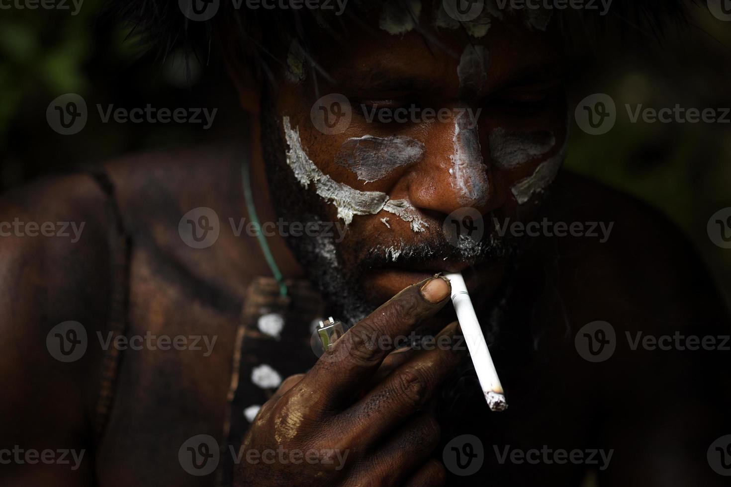 Close-up of painted face Dani tribe Papua man is smoking a cigarrette. photo