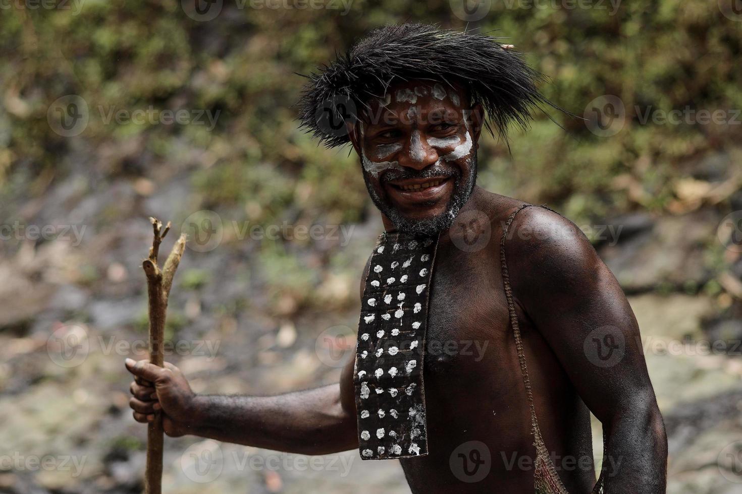 Potrait of Dani tribe man from Wamena Papua Indonesia wearing traditional clothes for hunting is smiling against blurred greenery forest background. photo