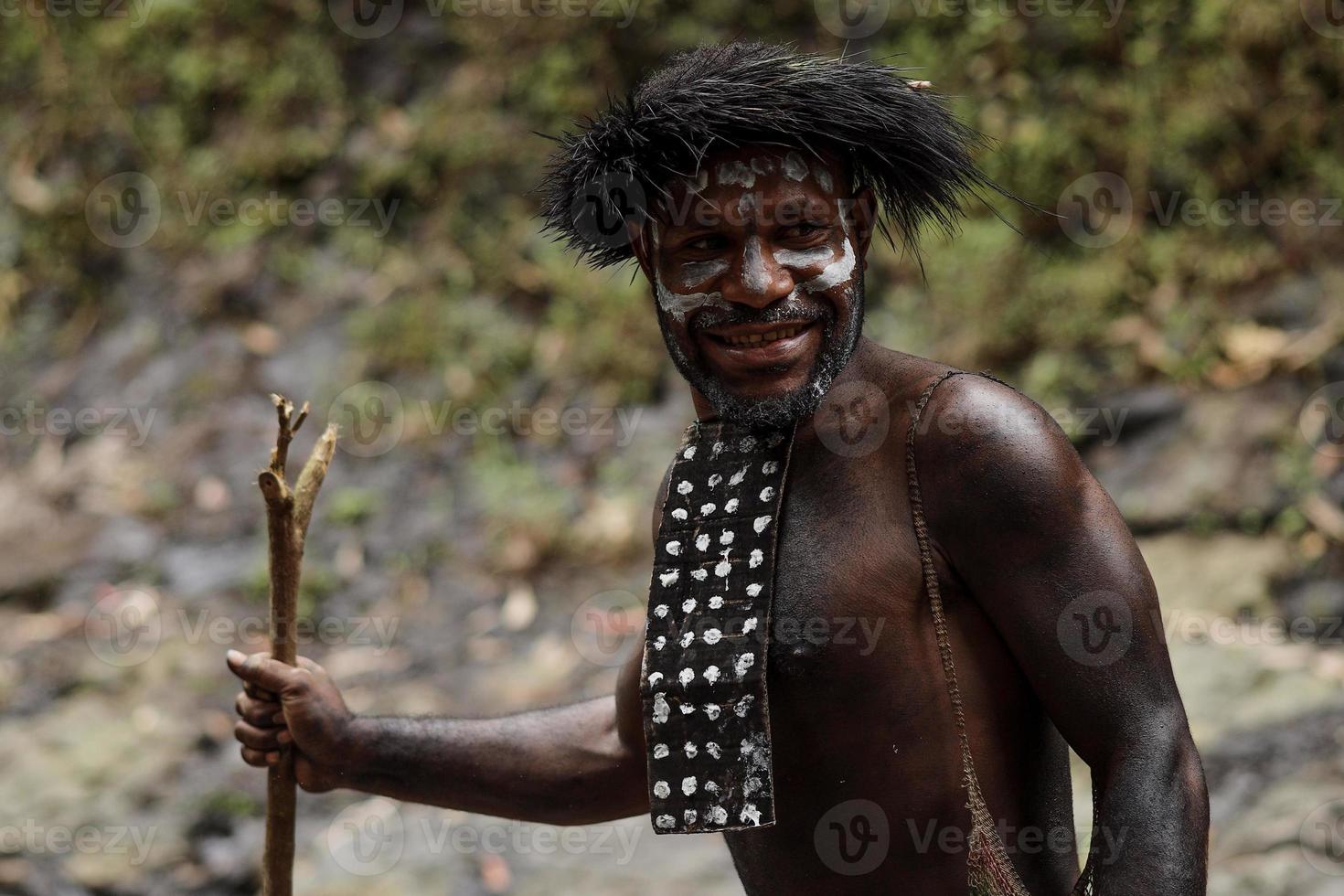 Potrait of Dani tribe man from Wamena Papua Indonesia wearing traditional clothes for hunting is smiling against blurred greenery forest background. photo