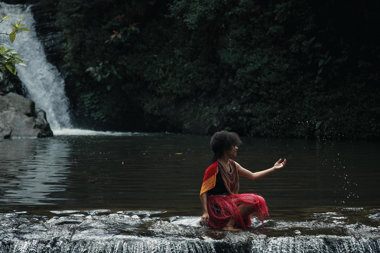 Wamena, Papua, INDONESIA, June 01, 2022 Attractive papua young girl  of dani tribe in traditional clothes is sitting and playing water against nature background. photo