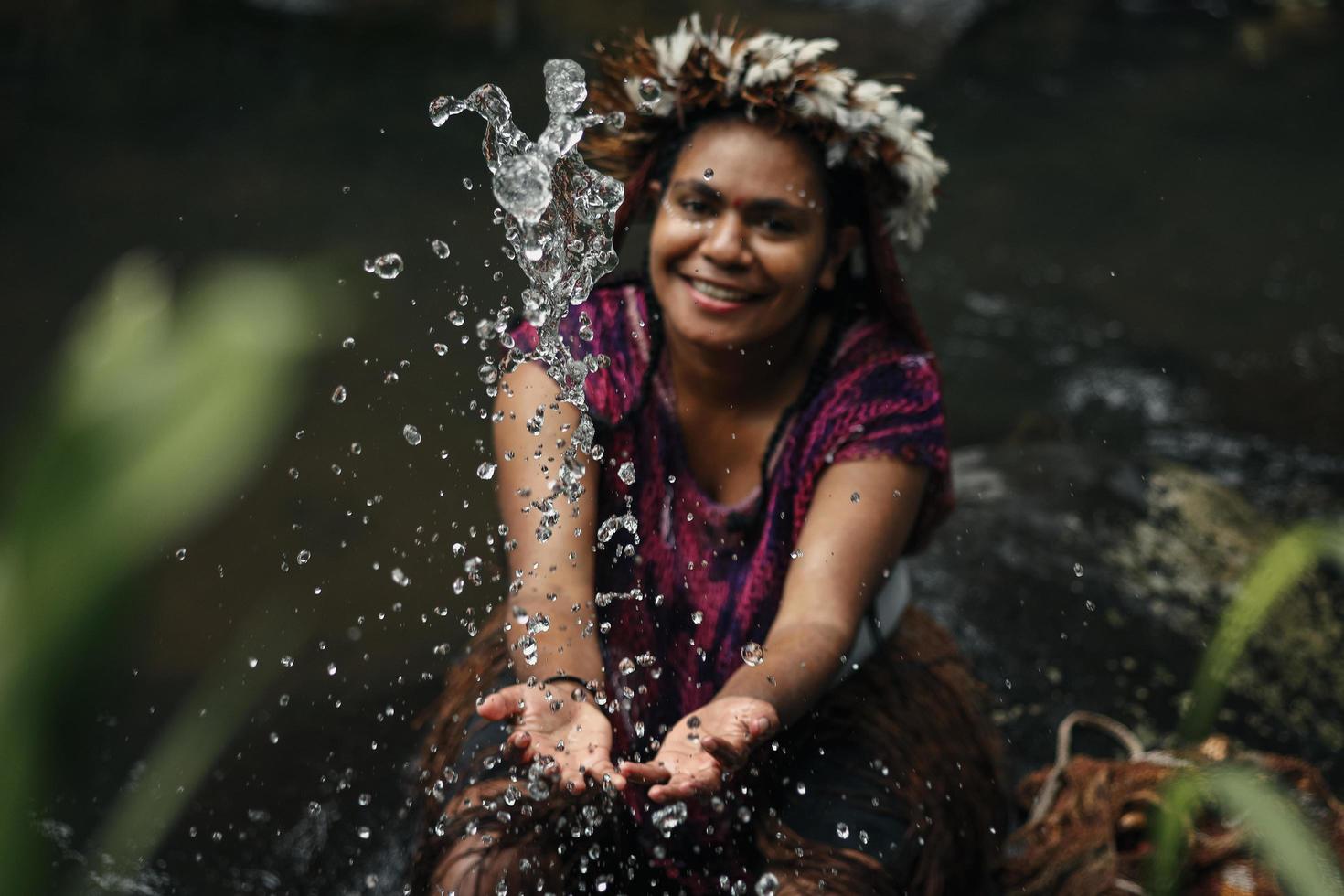 Wamena, Papua, INDONESIA, June 01, 2022 Close-up splash water against blurred background of young woman papuan tribe using feather crown in the river. photo