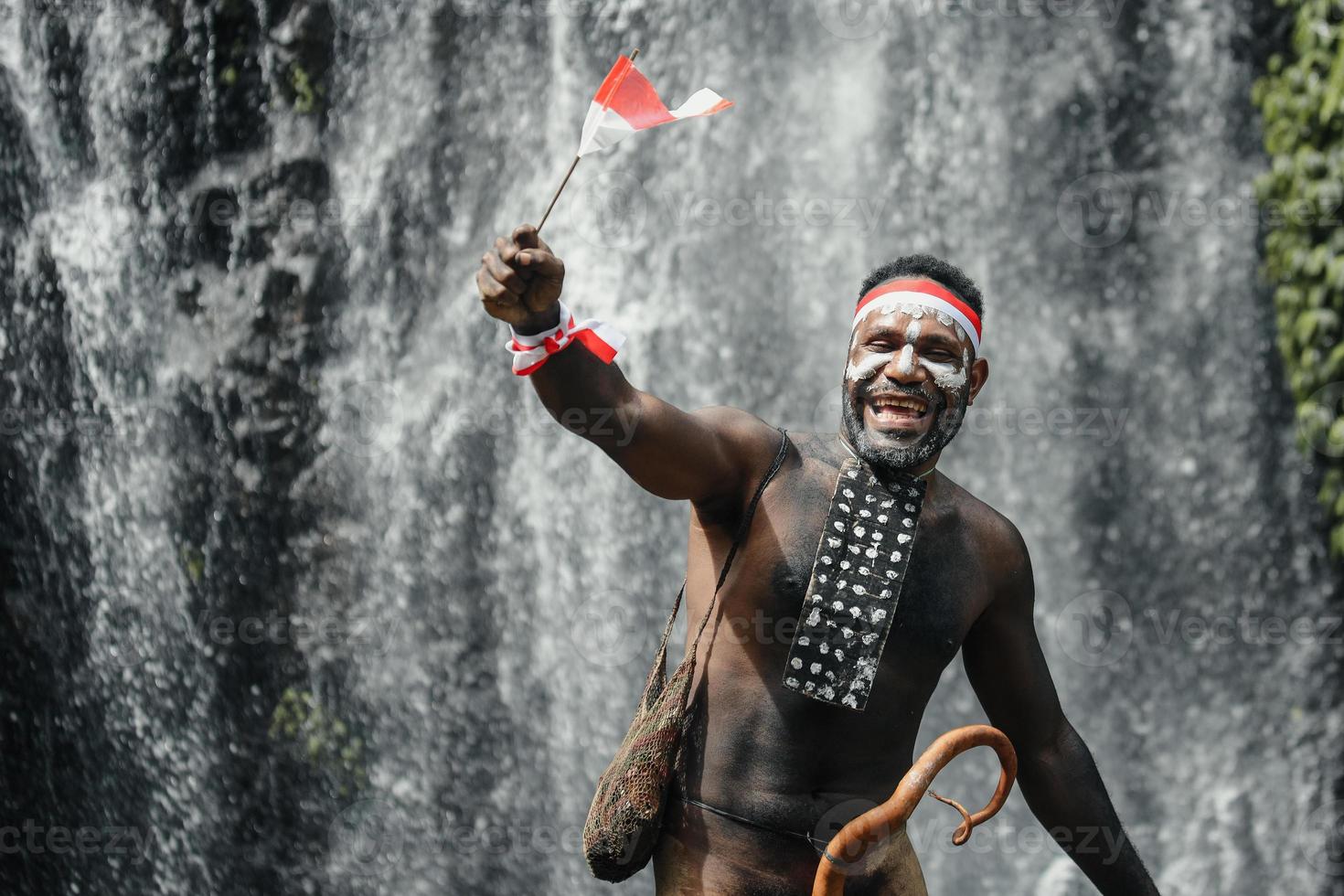 Papua man of Dani tribe is smiling and celebrating Indonesia independence day against waterfall background. photo
