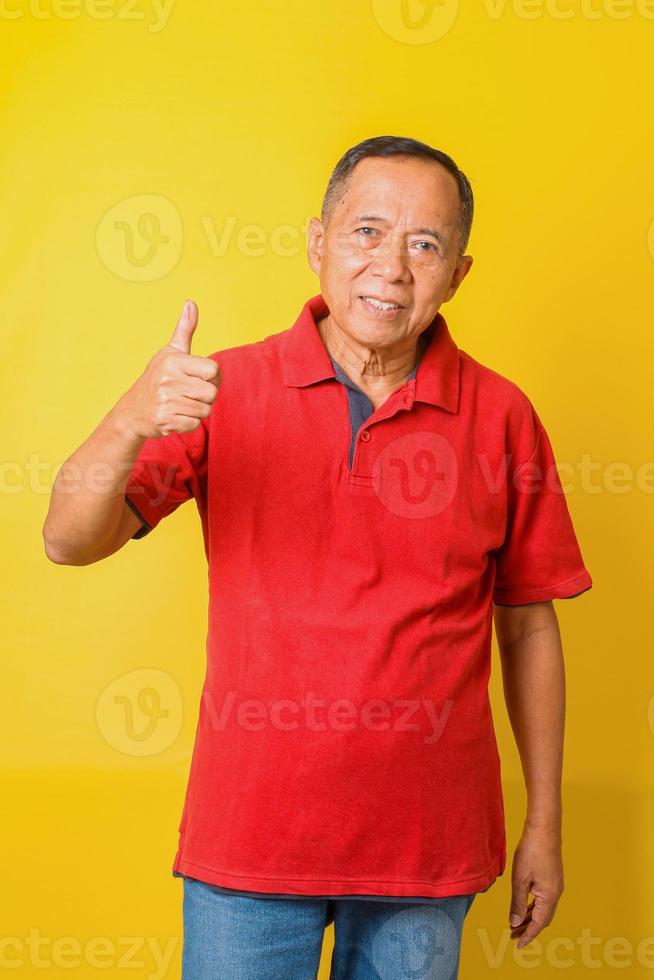 Asian senior man wearing casual t-shirt standing over isolated yellow background doing like thumbs up gesture with hand. Approving expression looking at the camera showing success. photo