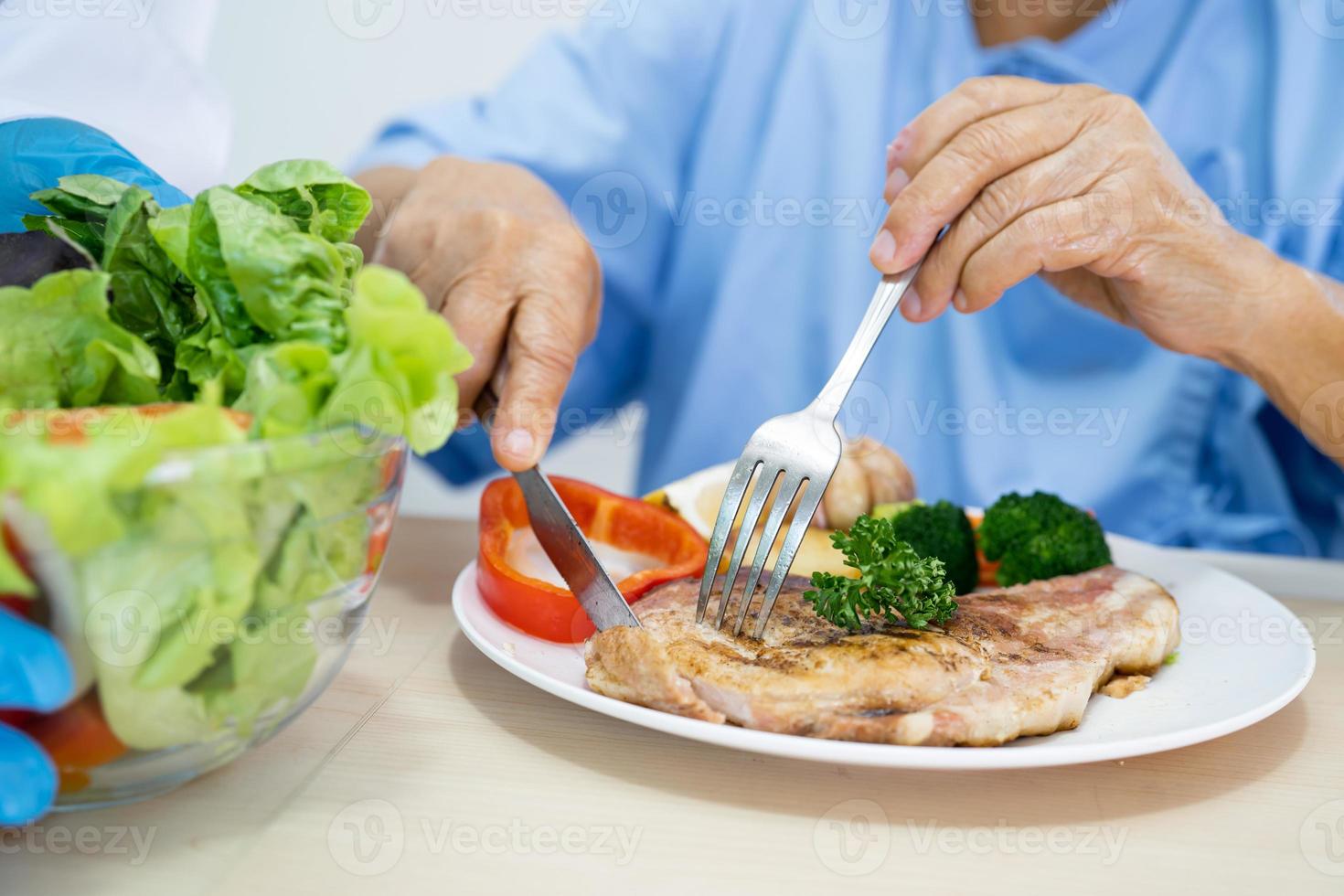 Asian senior or elderly old lady woman patient eating breakfast and vegetable healthy food with hope and happy while sitting and hungry on bed in hospital. photo