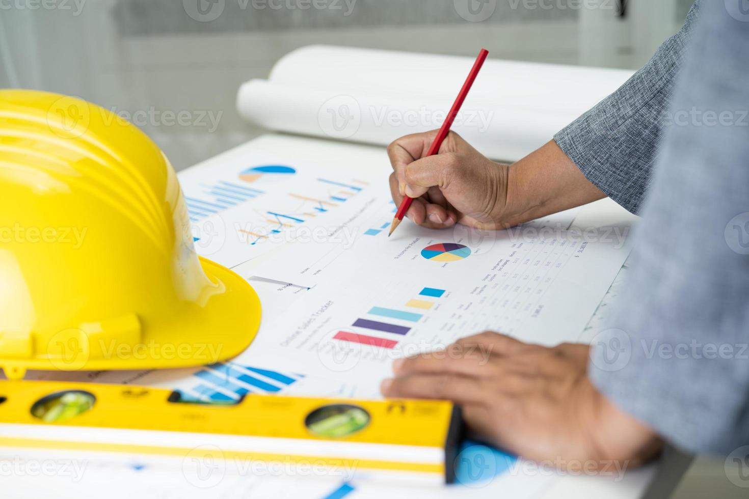 Asian engineer with architectural house plan project blueprint, graph and yellow helmet and engineering construction tools. photo