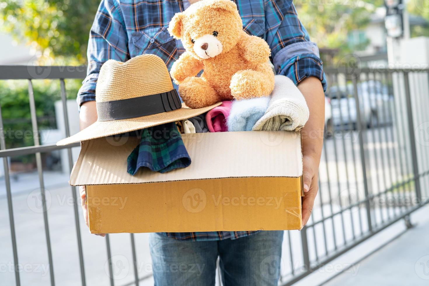 Holding clothing donation box with used clothes and doll at home to support help for poor people in the world. photo