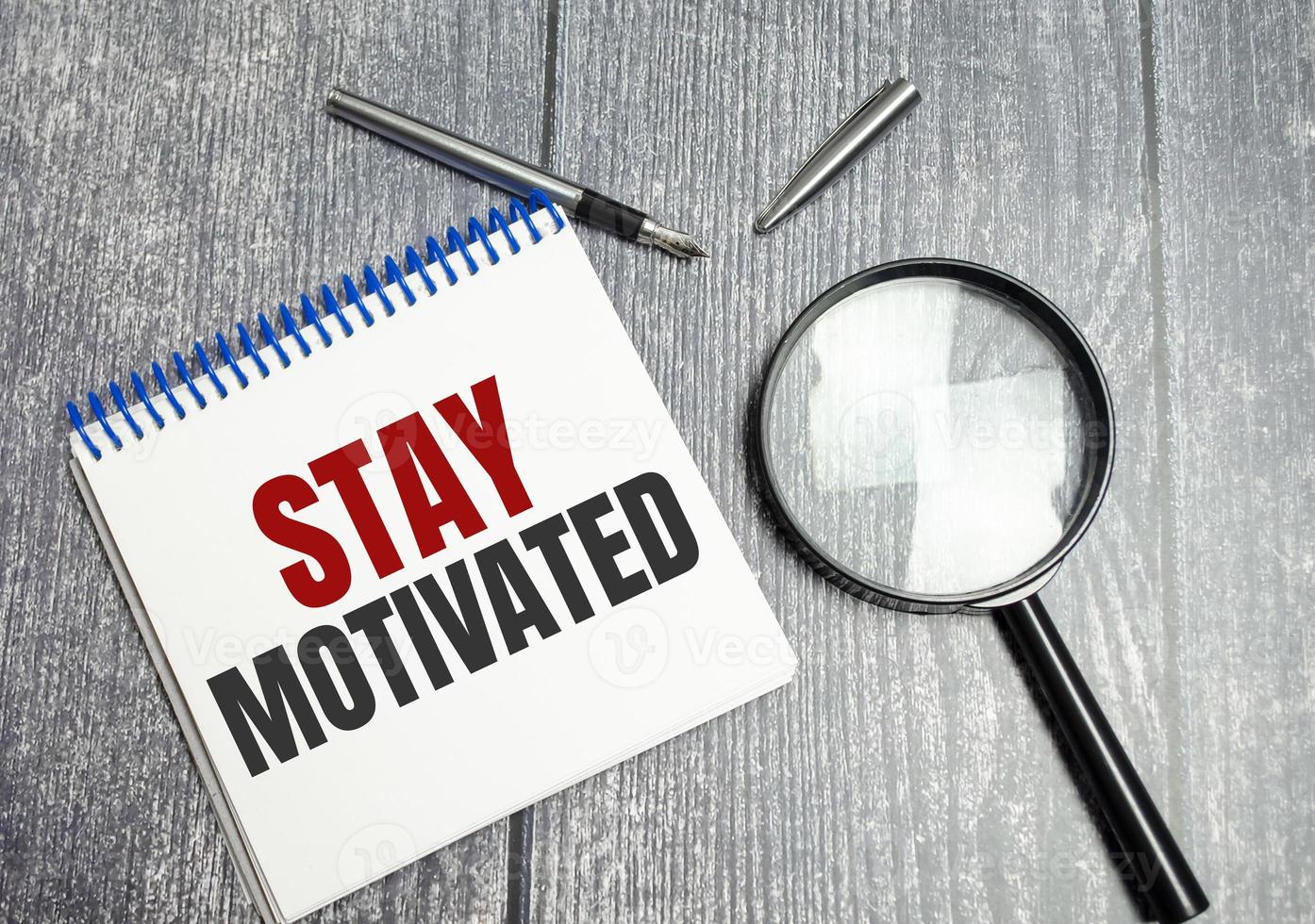 stay motivated words on notepad and wooden background and magnifier photo