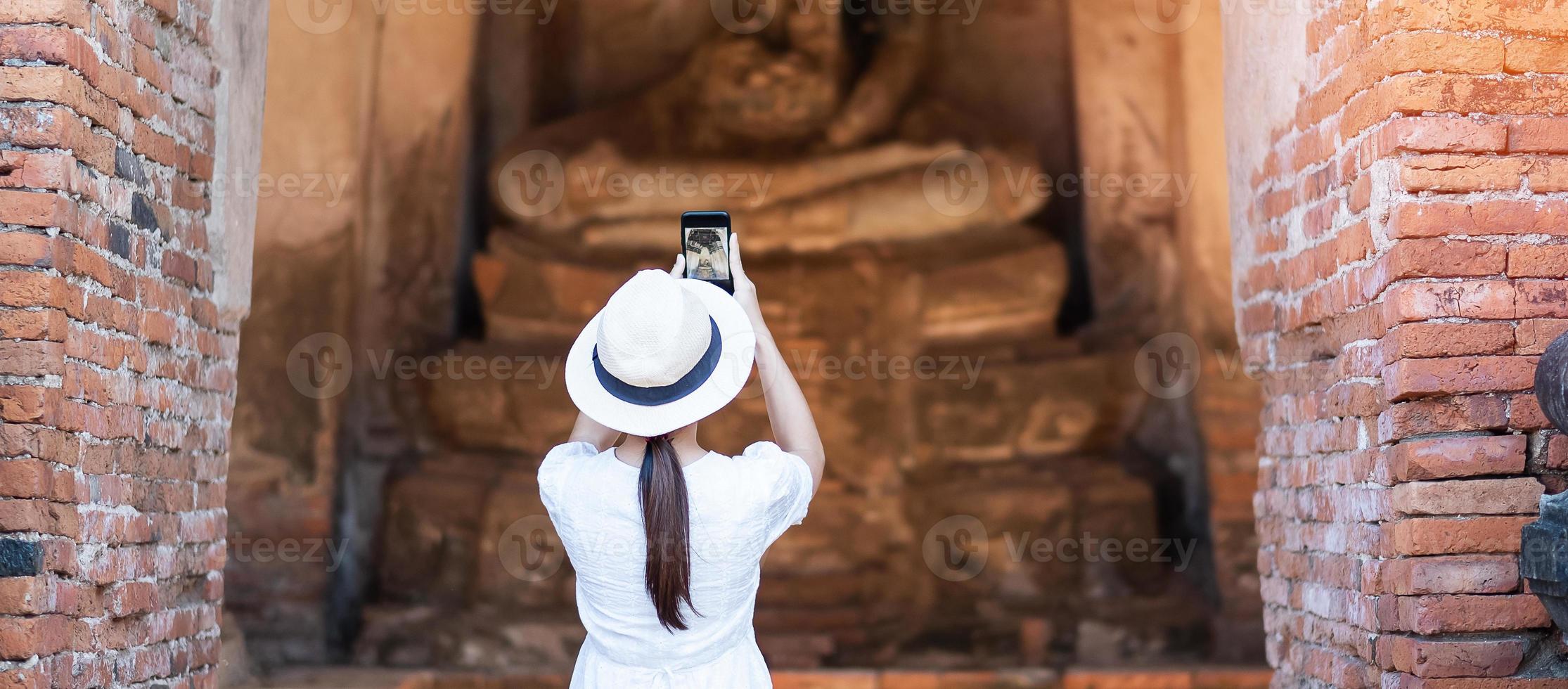 mujer turista feliz vestida de blanco tomando fotos con un teléfono inteligente móvil, durante su visita al templo wat chaiwatthanaram en el parque histórico de ayutthaya, concepto de viaje de verano, solo, asia y tailandia