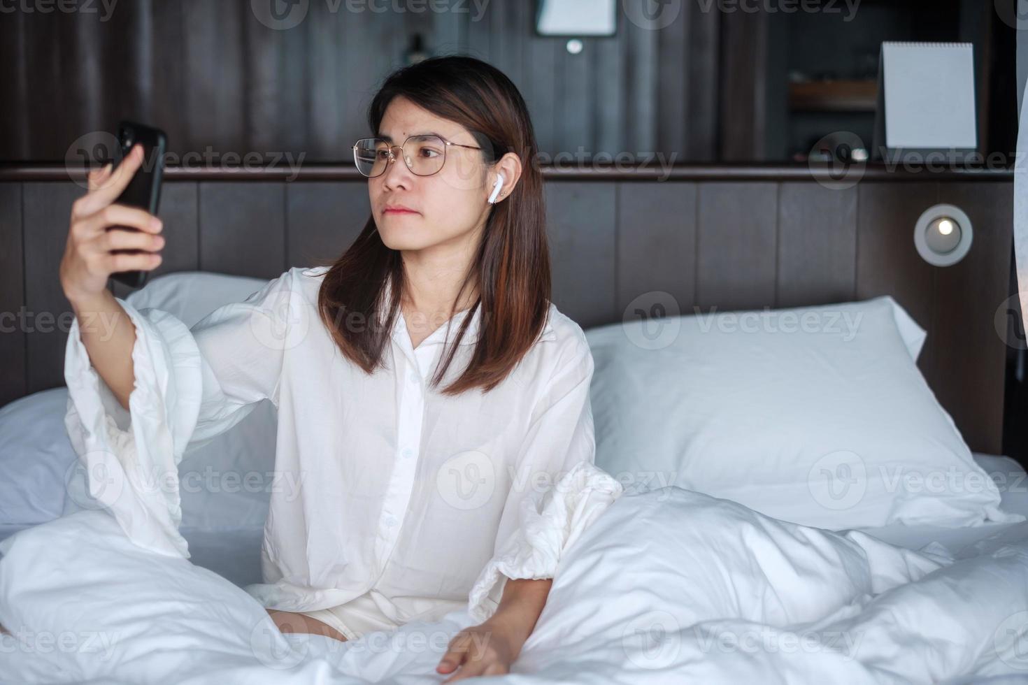 Happy woman using smart phone for video call, female meeting  online by mobile phone on bed. technology, network, work from home, lifestyle and digital communication concept photo