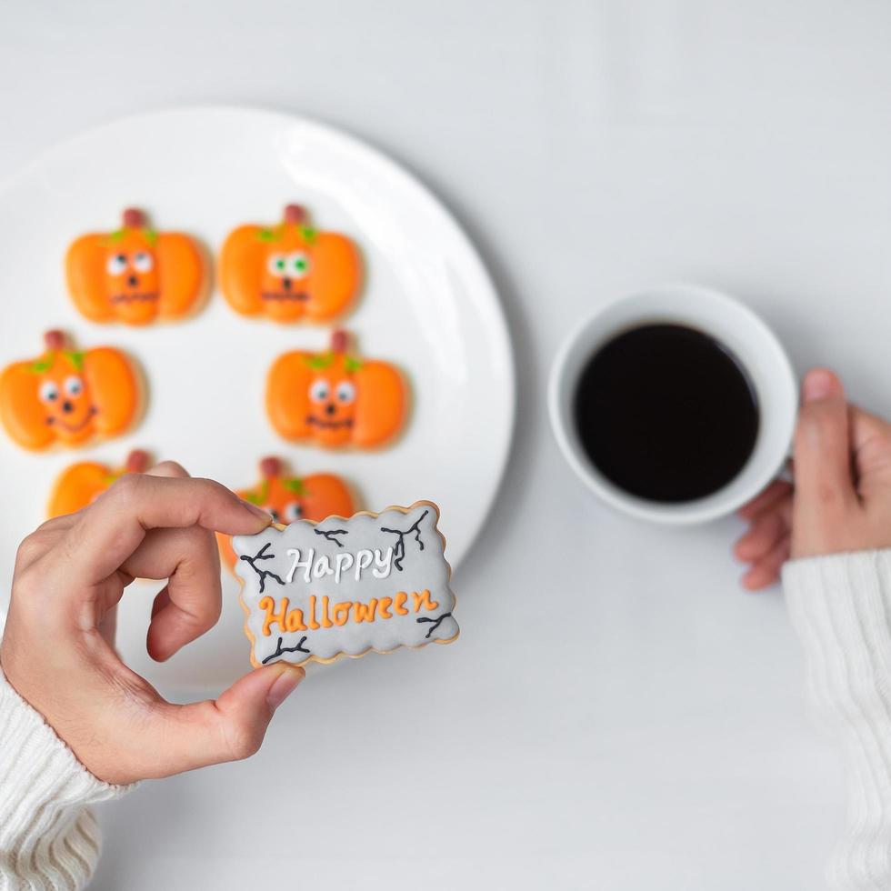 woman hand holding funny Halloween Cookie during drinking coffee. Happy Halloween day, Trick or Threat, Hello October, fall autumn, Traditional, party and holiday concept photo
