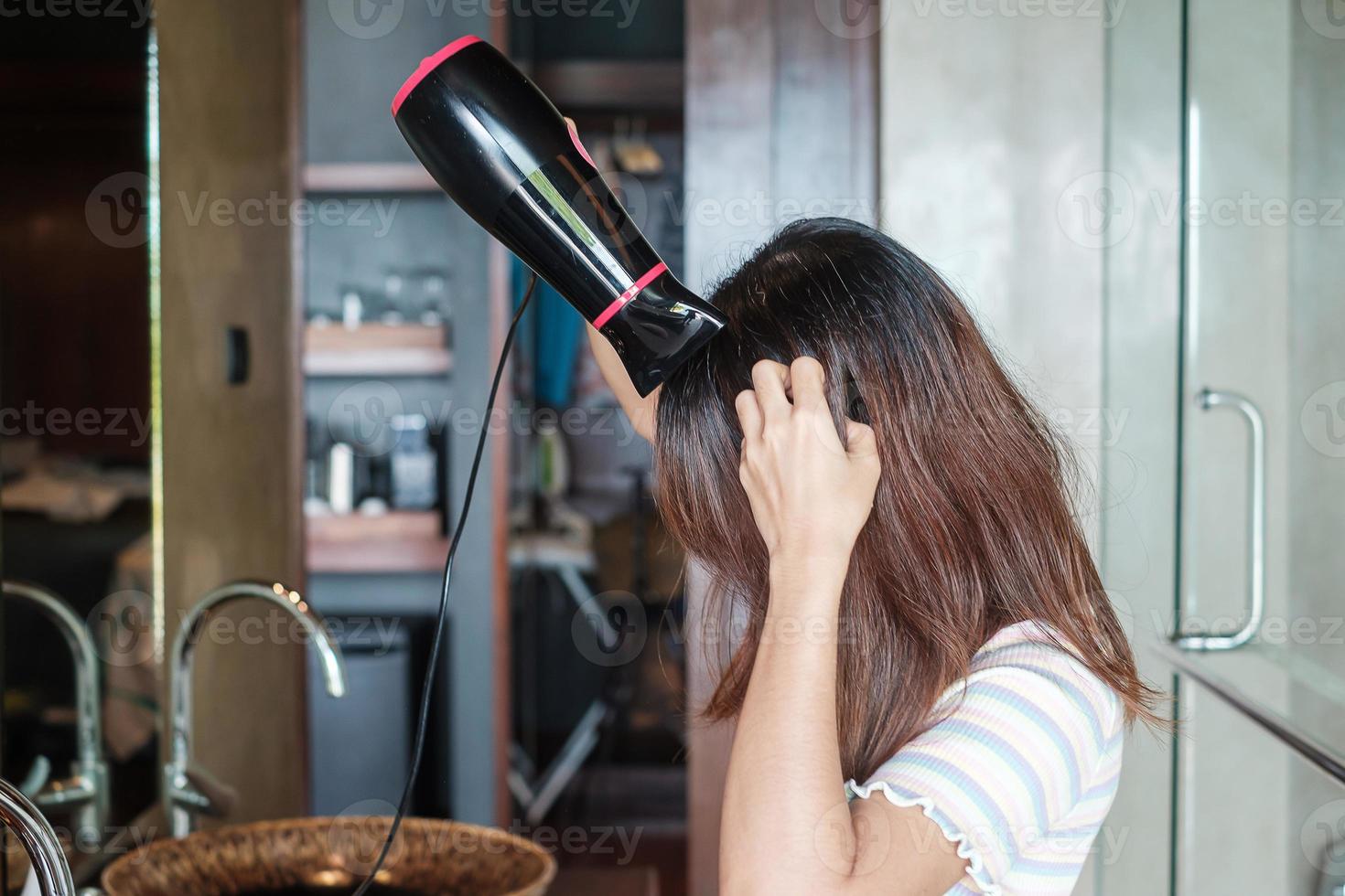 young woman using hair dryer near mirror at home or hotel. Hairstyles and lifestyle concepts photo