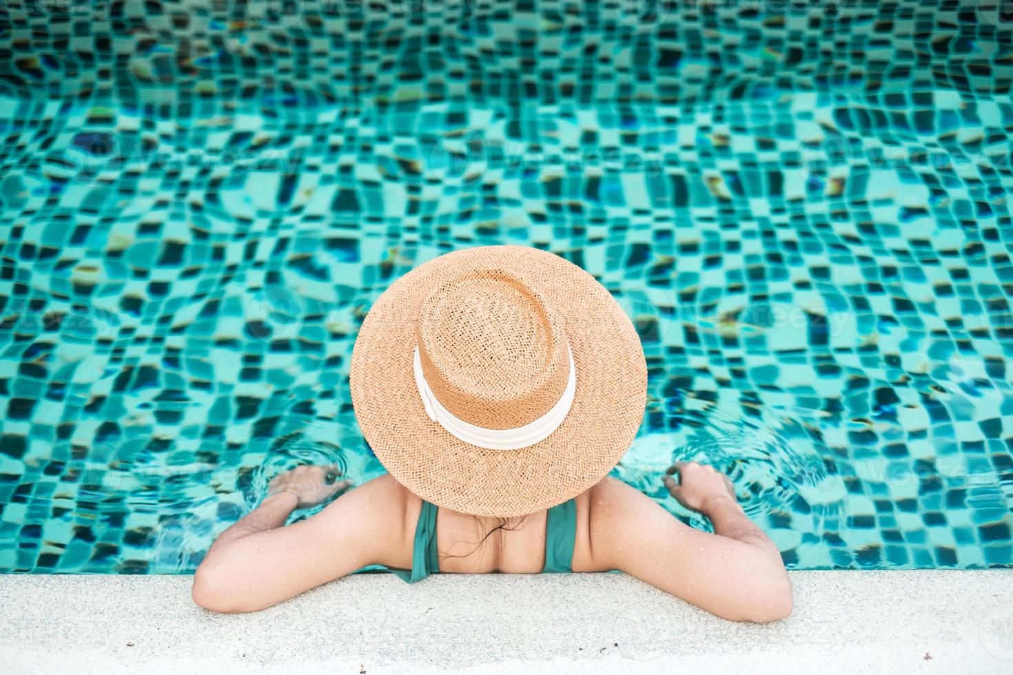 mujer feliz en traje de baño verde y sombrero en la piscina en un hotel de lujo frente al mar. mujer joven disfruta en un resort tropical. concepto de relajación, verano, viajes, vacaciones, vacaciones y fin de semana foto