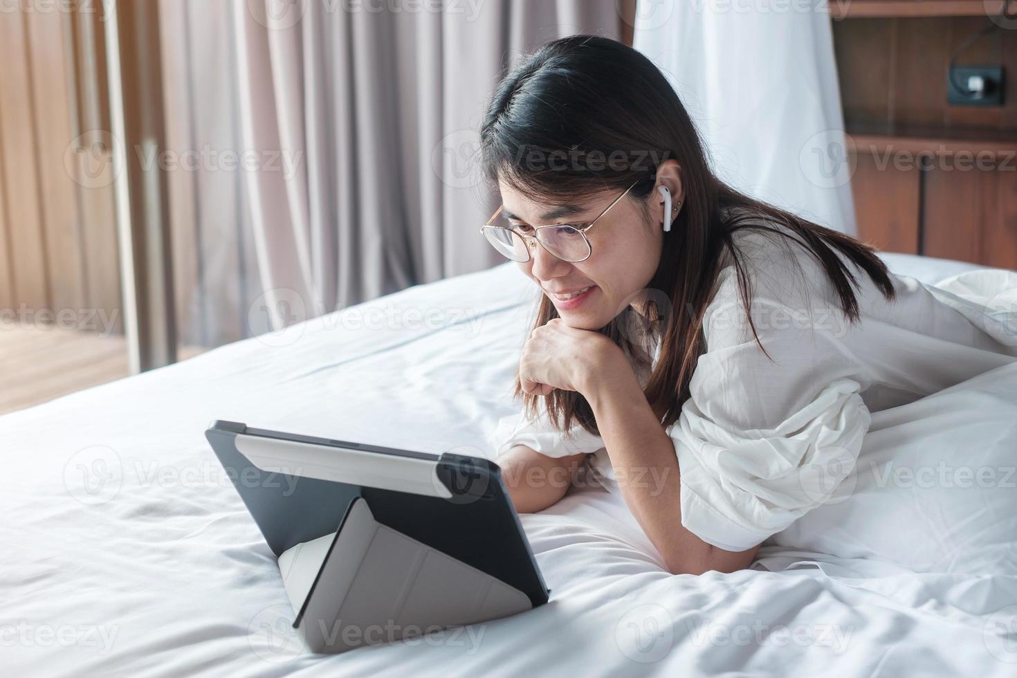 Happy woman using tablet for social media, young female watching movies on computer pad on bed at home. technology, network, online shopping, e commerce, lifestyle and digital communication concept photo