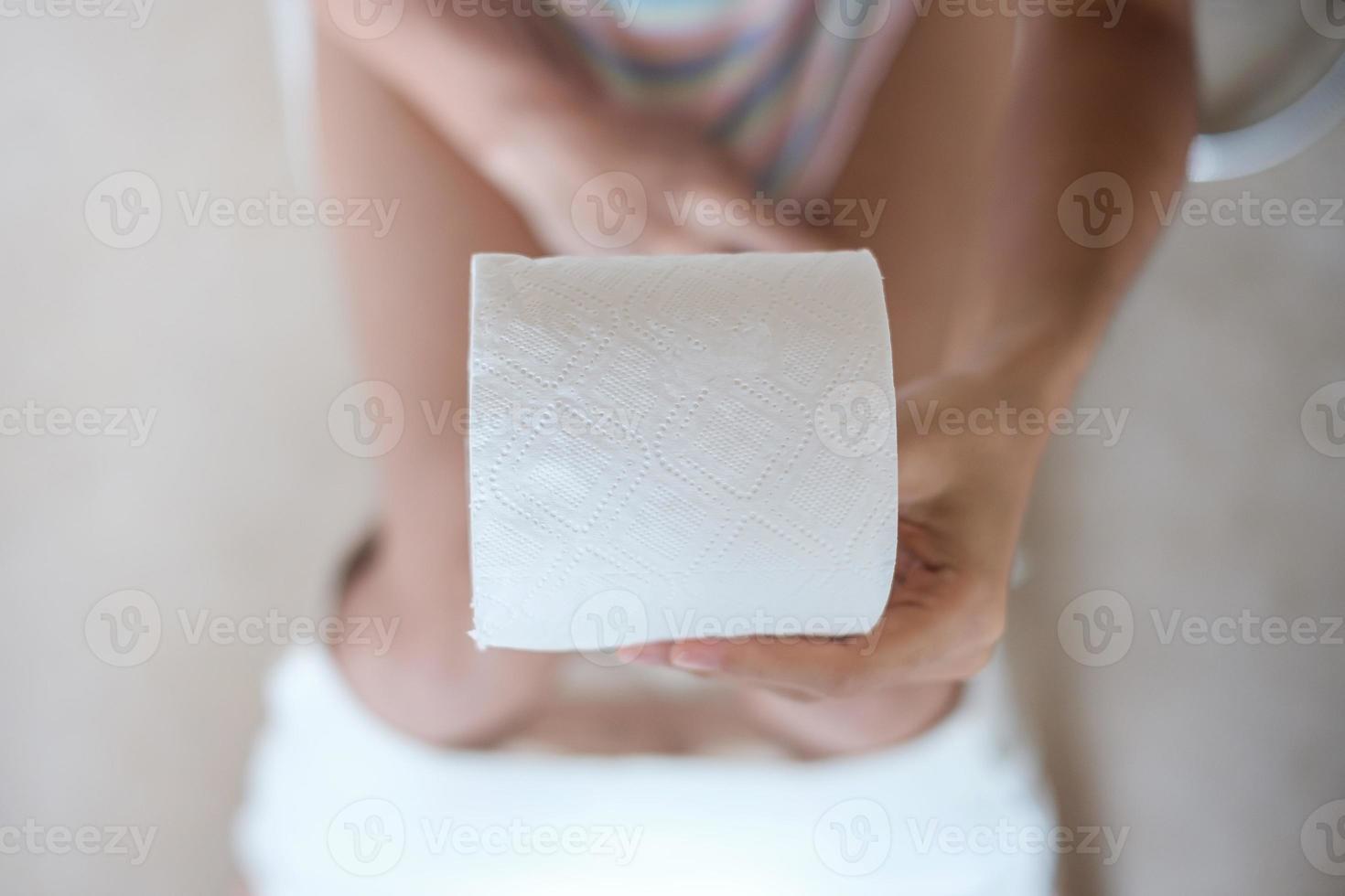 Woman holding toilet paper roll during sit on toilet bowl diarrhea, constipated period, infection, Healthcare, Insurance, Medical concept photo