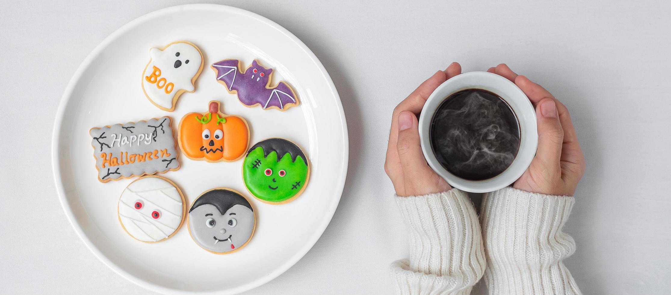 woman hand holding coffee cup during eating funny Halloween Cookies. Happy Halloween day, Trick or Threat, Hello October, fall autumn, Traditional, party and holiday concept photo