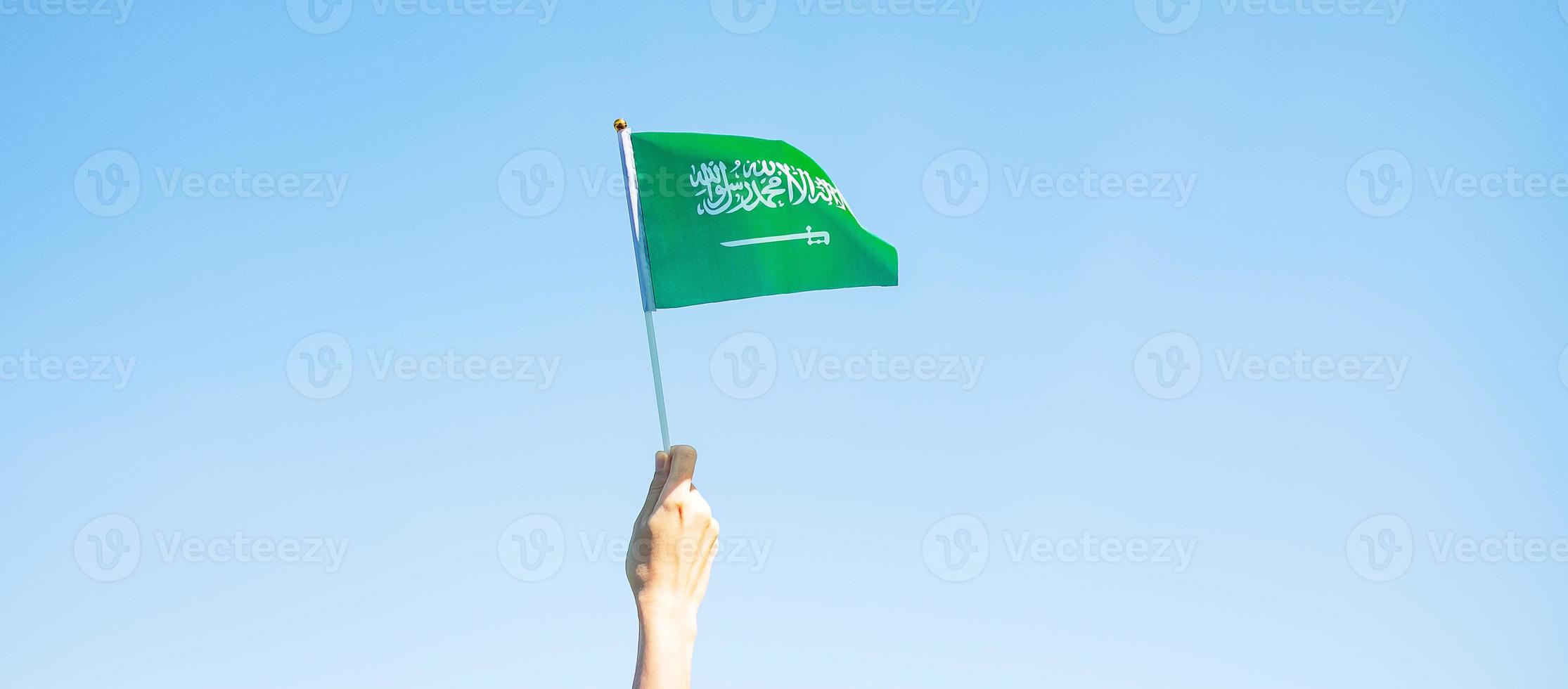 hand holding Saudi Arabia flag on blue sky background. September Saudi Arabia national day and Happy celebration concepts photo