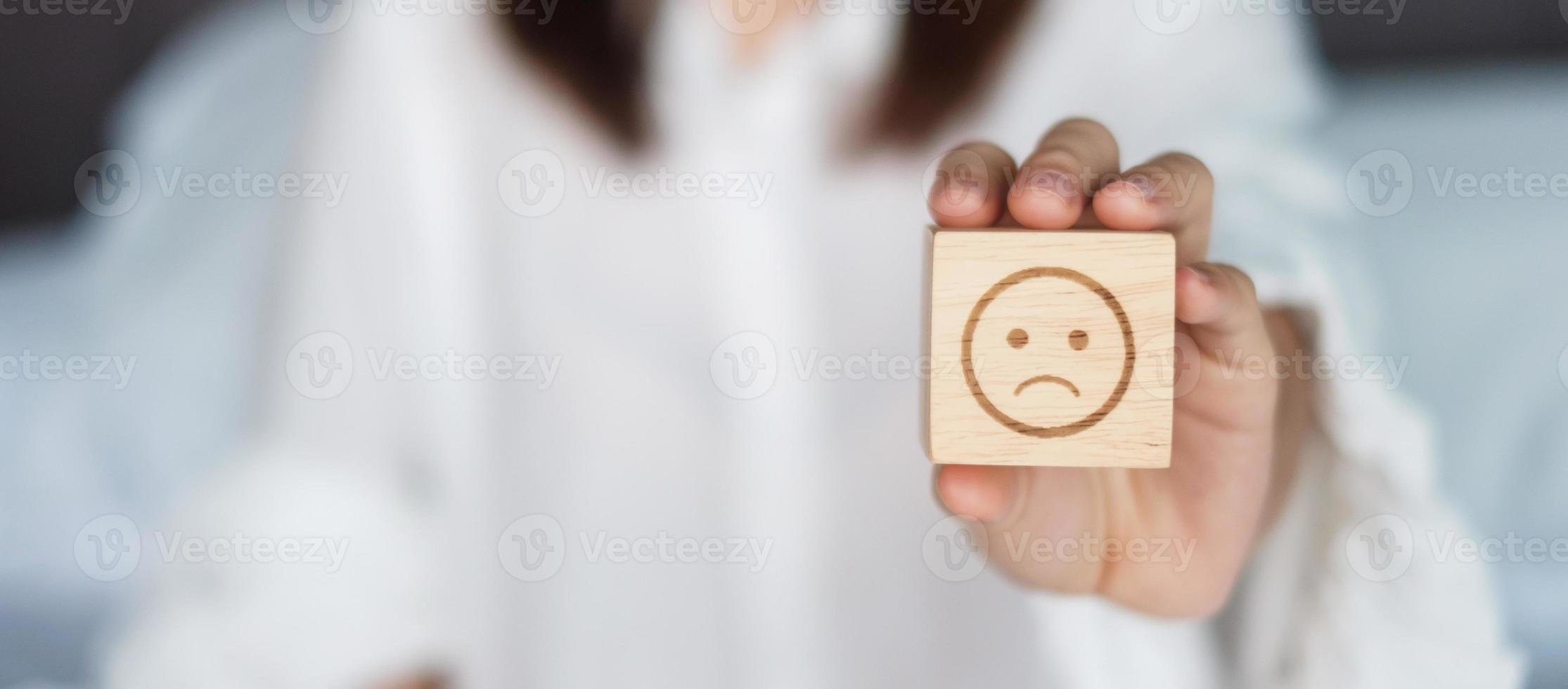 mujer sosteniendo un bloque de cara de emoción enojada. el cliente elige el emoticono para las opiniones de los usuarios. calificación de servicio, salud mental, pensamiento positivo, satisfacción, evaluación y concepto de retroalimentación foto