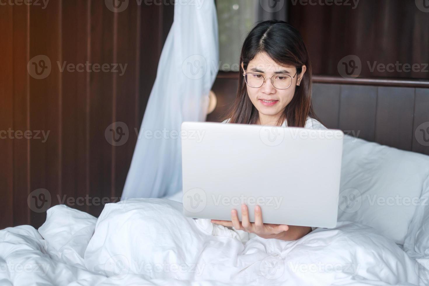 Happy woman using laptop for work, female meeting  online by computer notebook on bed. technology, network, work from home, lifestyle and digital communication concept photo