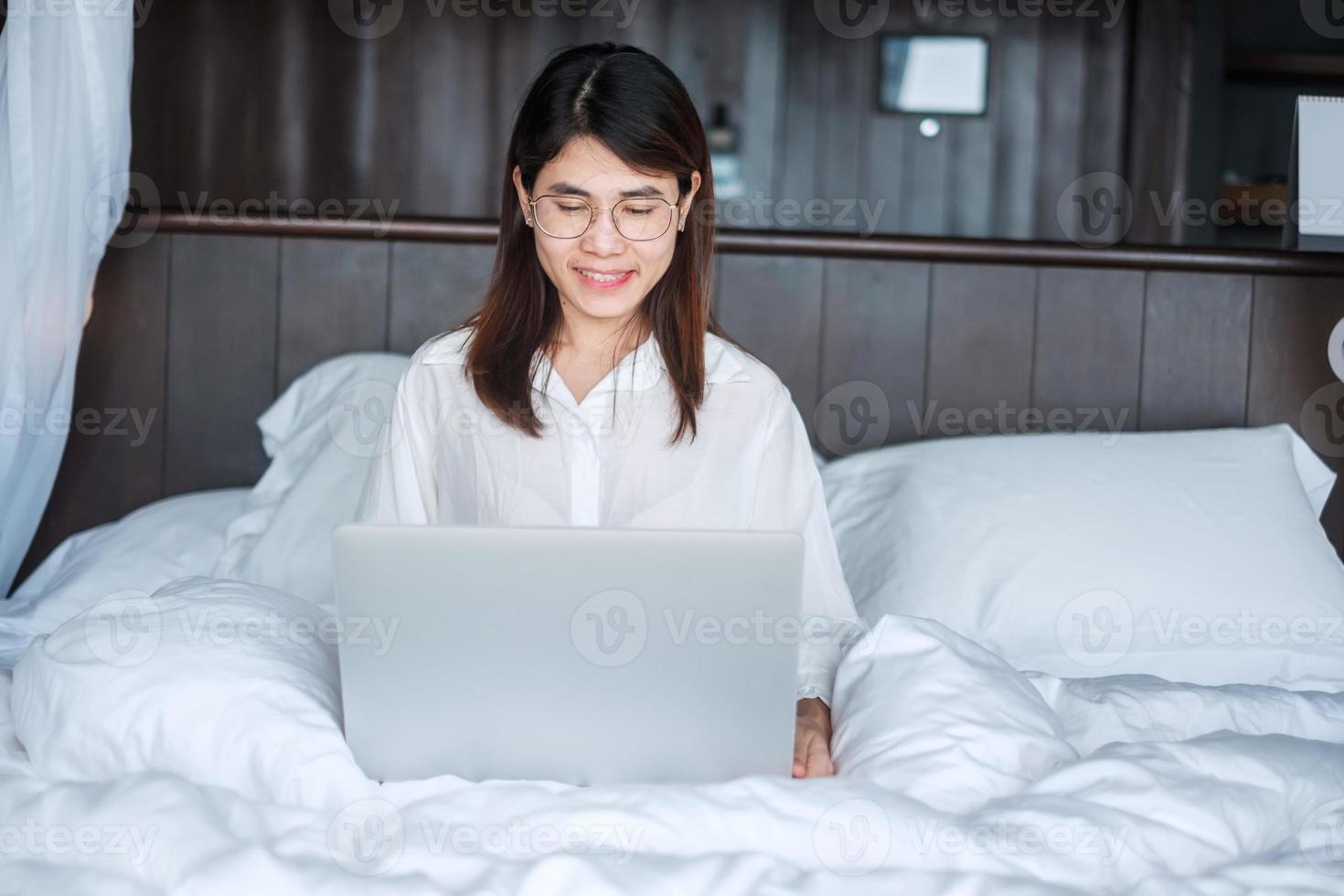 Happy woman using laptop for work, female meeting  online by computer notebook on bed. technology, network, work from home, lifestyle and digital communication concept photo