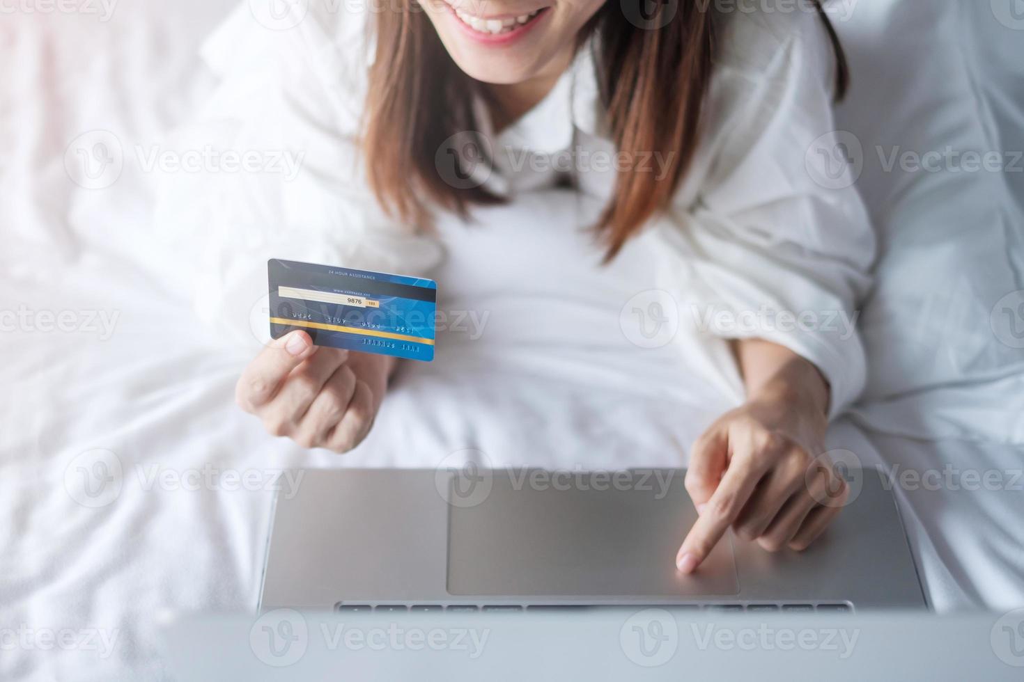 woman using computer laptop and credit card for online shopping while making order on bed in morning at home. technology, ecommerce, digital banking online payment and apartment living concept photo