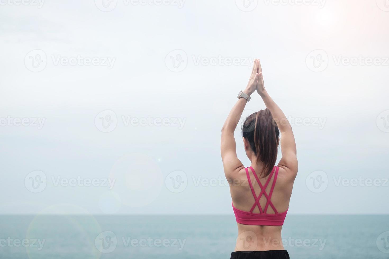 mujer joven haciendo yoga y estirando músculos por la mañana, meditación de niña sana contra la vista al mar. conceptos de bienestar, fitness, vitalidad, ejercicio y equilibrio entre la vida laboral y personal foto