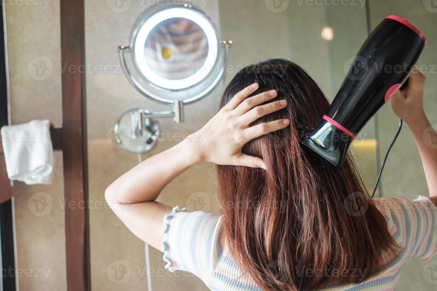 mujer joven que usa secador de pelo cerca del espejo en casa o en el hotel. peinados y conceptos de estilo de vida foto