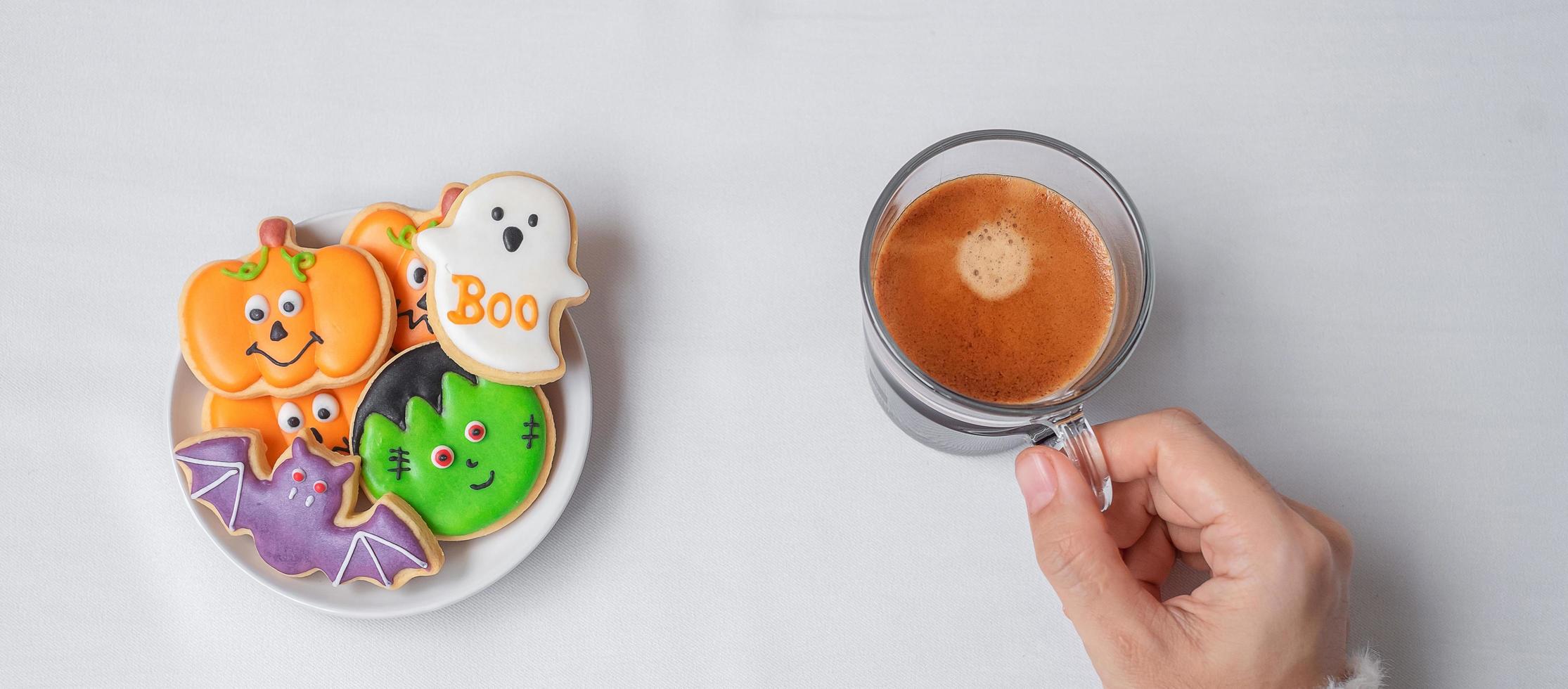 mano de mujer sosteniendo la taza de café durante la comida divertidas galletas de halloween. feliz día de halloween, truco o amenaza, hola octubre, otoño otoño, tradicional, concepto de fiesta y vacaciones foto