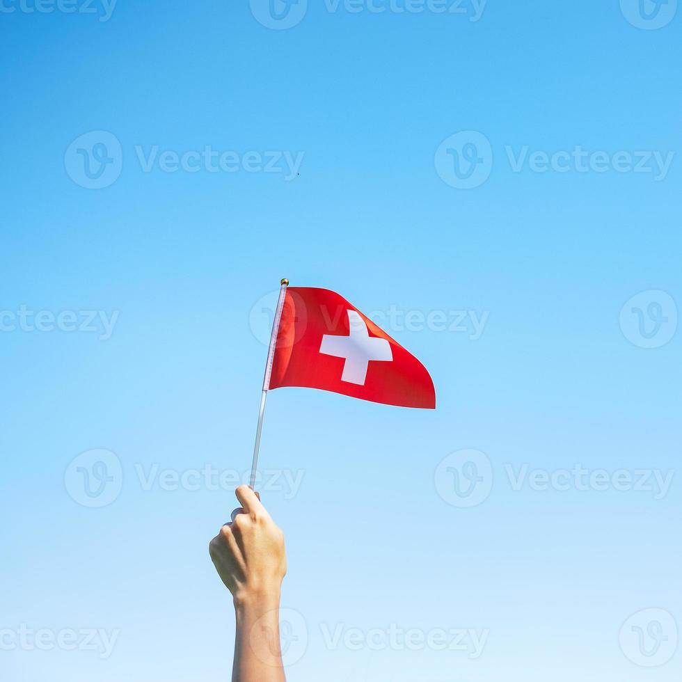 hand holding Switzerland flag on blue sky background. Switzerland National Day and happy celebration concepts photo
