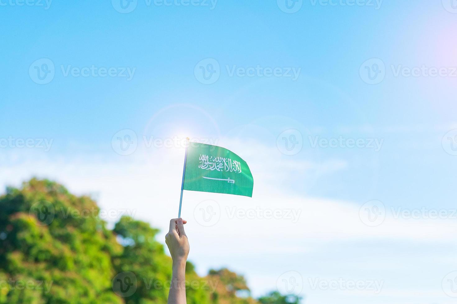 mano sosteniendo la bandera de arabia saudita sobre fondo de cielo azul. septiembre día nacional de arabia saudita y conceptos de celebración feliz foto