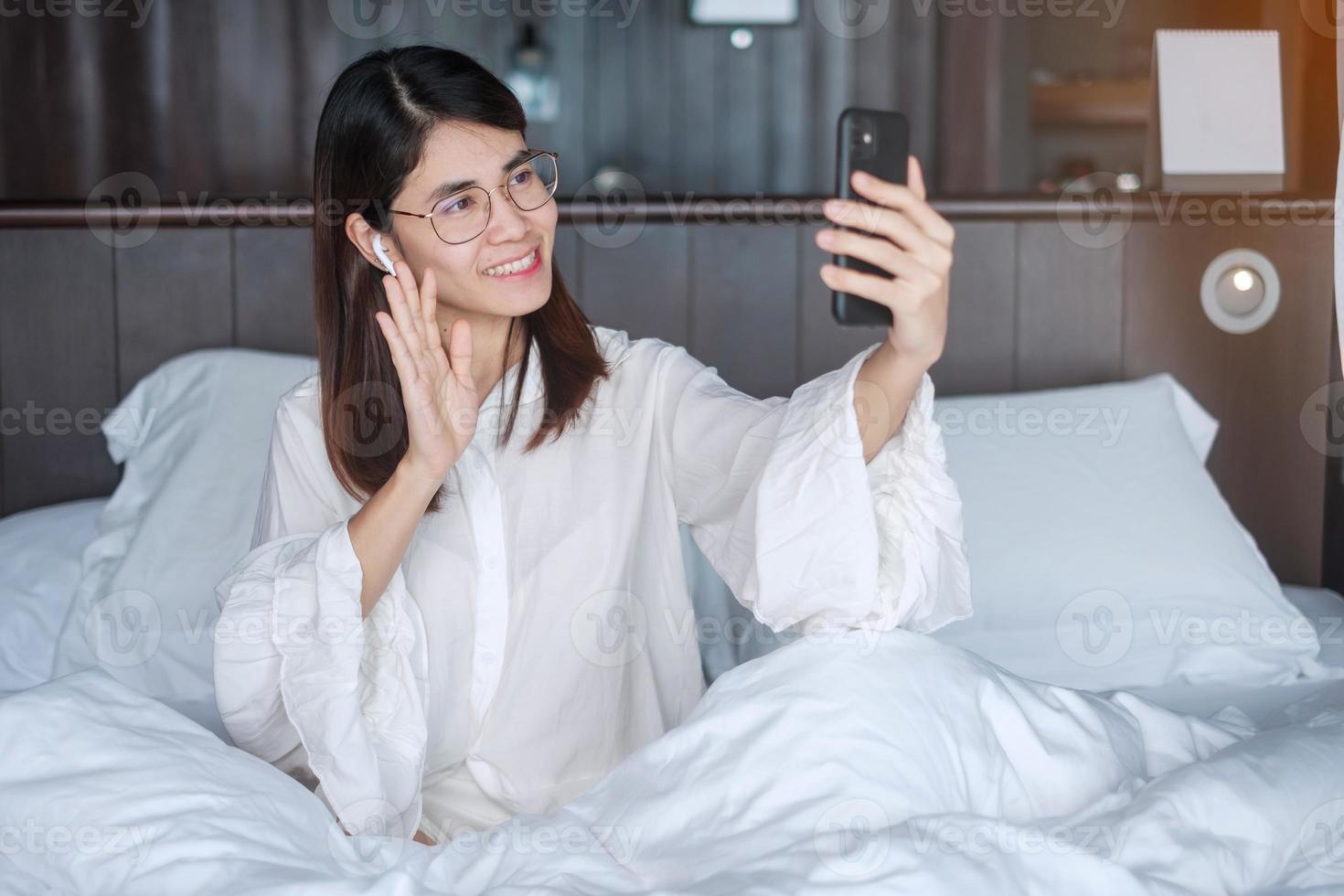 Happy woman using smart phone for video call, female meeting  online by mobile phone on bed. technology, network, work from home, lifestyle and digital communication concept photo