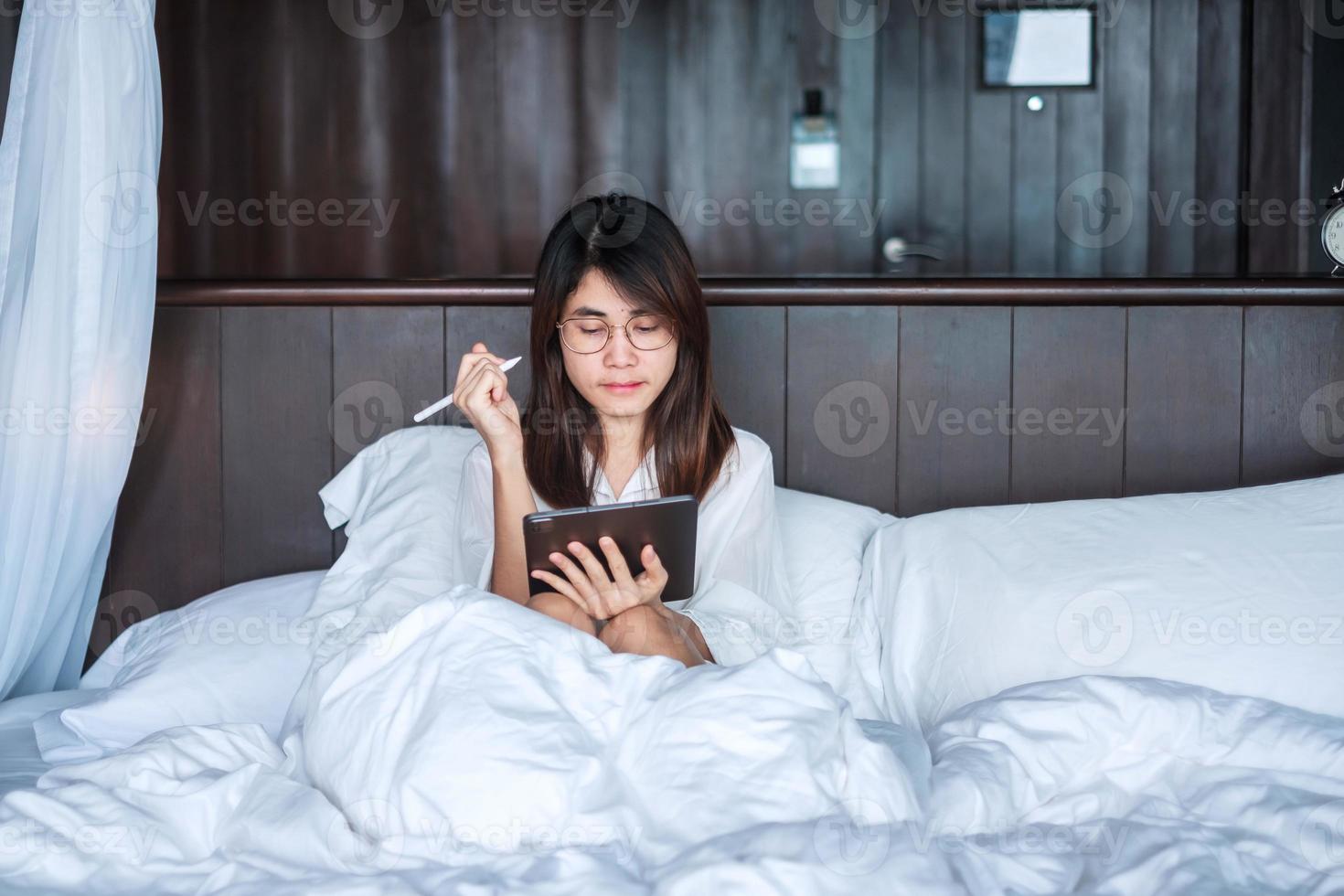 Happy woman using tablet for social media, young female watching movies on computer pad on bed at home. technology, network, online shopping, e commerce, lifestyle and digital communication concept photo