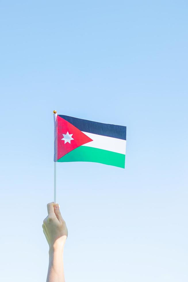 mano sosteniendo la bandera jordana en el fondo de la naturaleza. día de la independencia de jordania y conceptos de celebración feliz foto