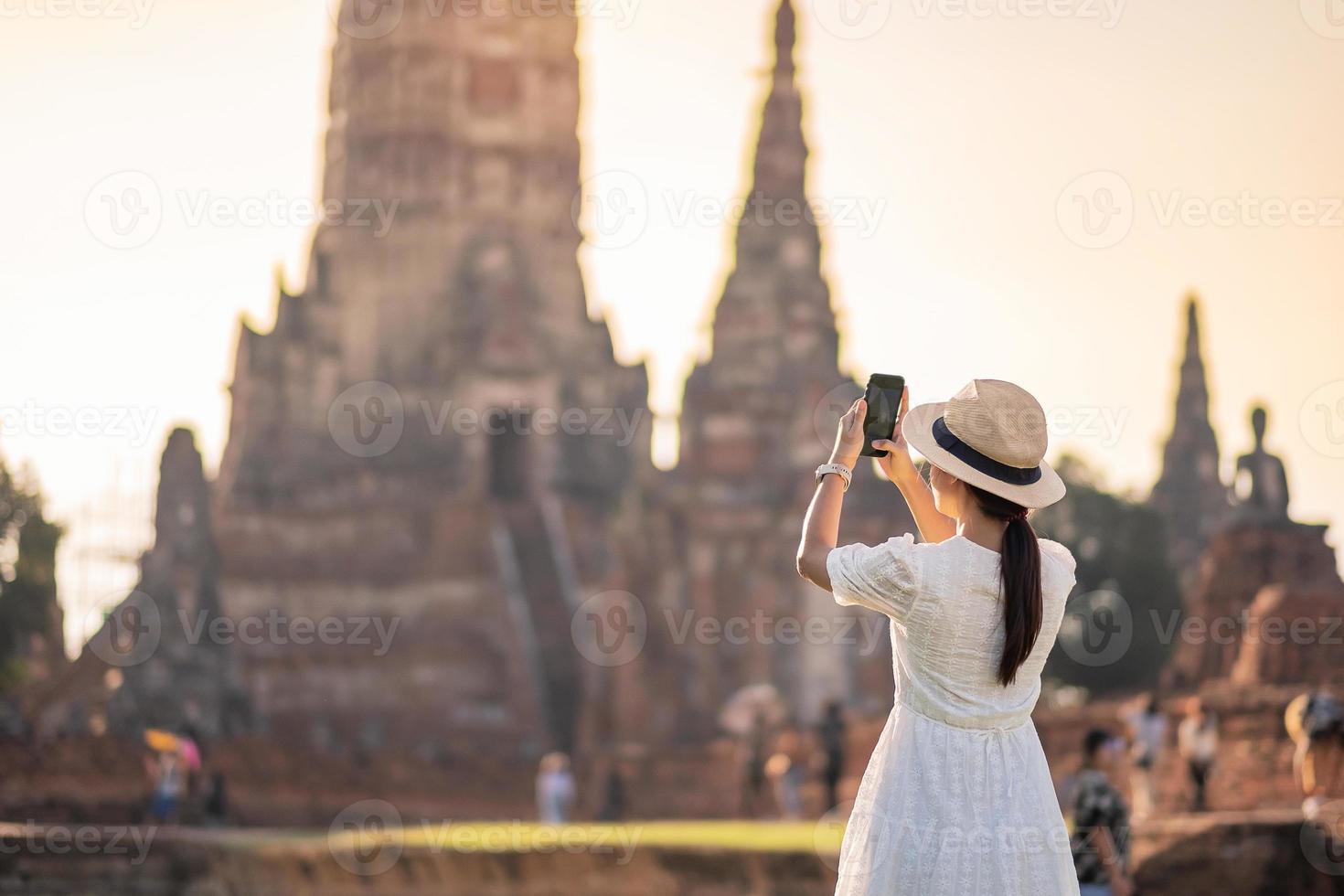 mujer turista feliz vestida de blanco tomando fotos con un teléfono inteligente móvil, durante su visita al templo wat chaiwatthanaram en el parque histórico de ayutthaya, concepto de viaje de verano, solo, asia y tailandia