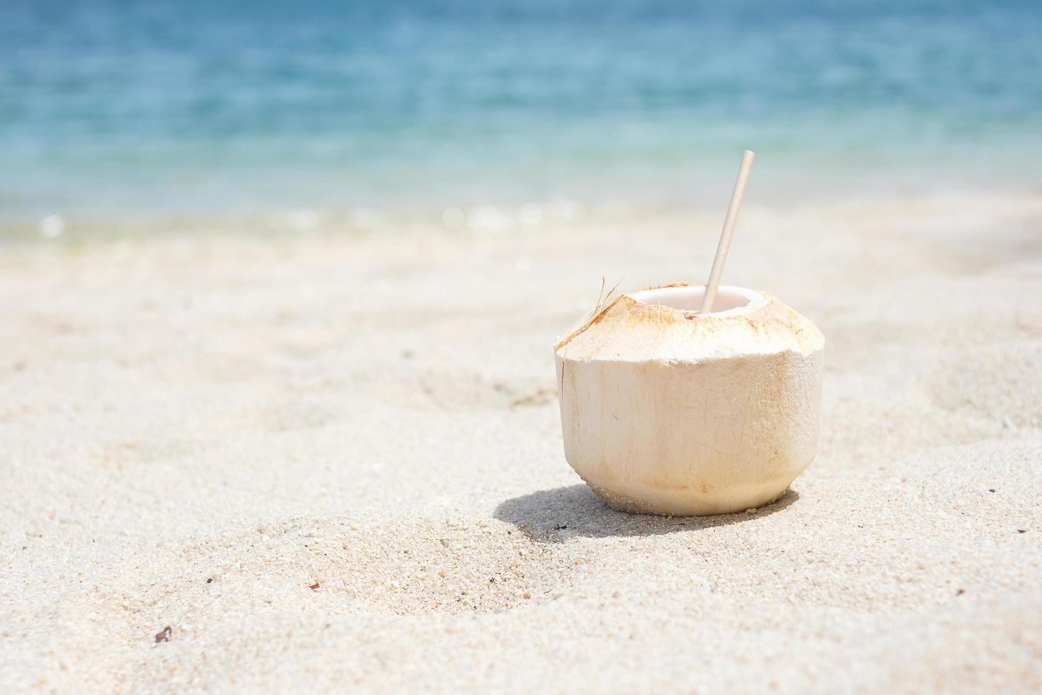 Fresh coconut juice and straw on white sand against tropical beach background. Summer, relaxing and vacation concepts photo