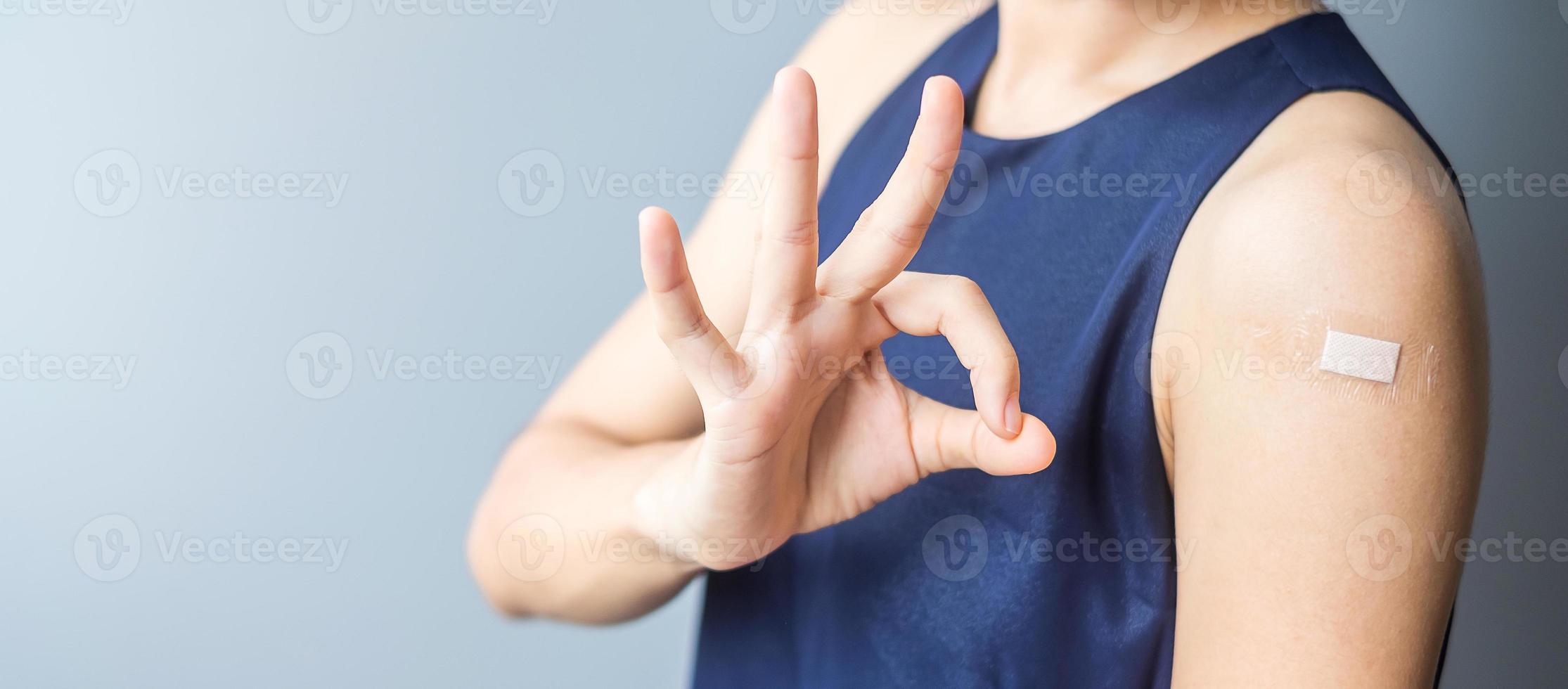 Happy woman showing OK sign with bandage after receiving covid 19 vaccine. Vaccination, herd immunity, side effect, efficiency, vaccine passport and Coronavirus pandemic photo