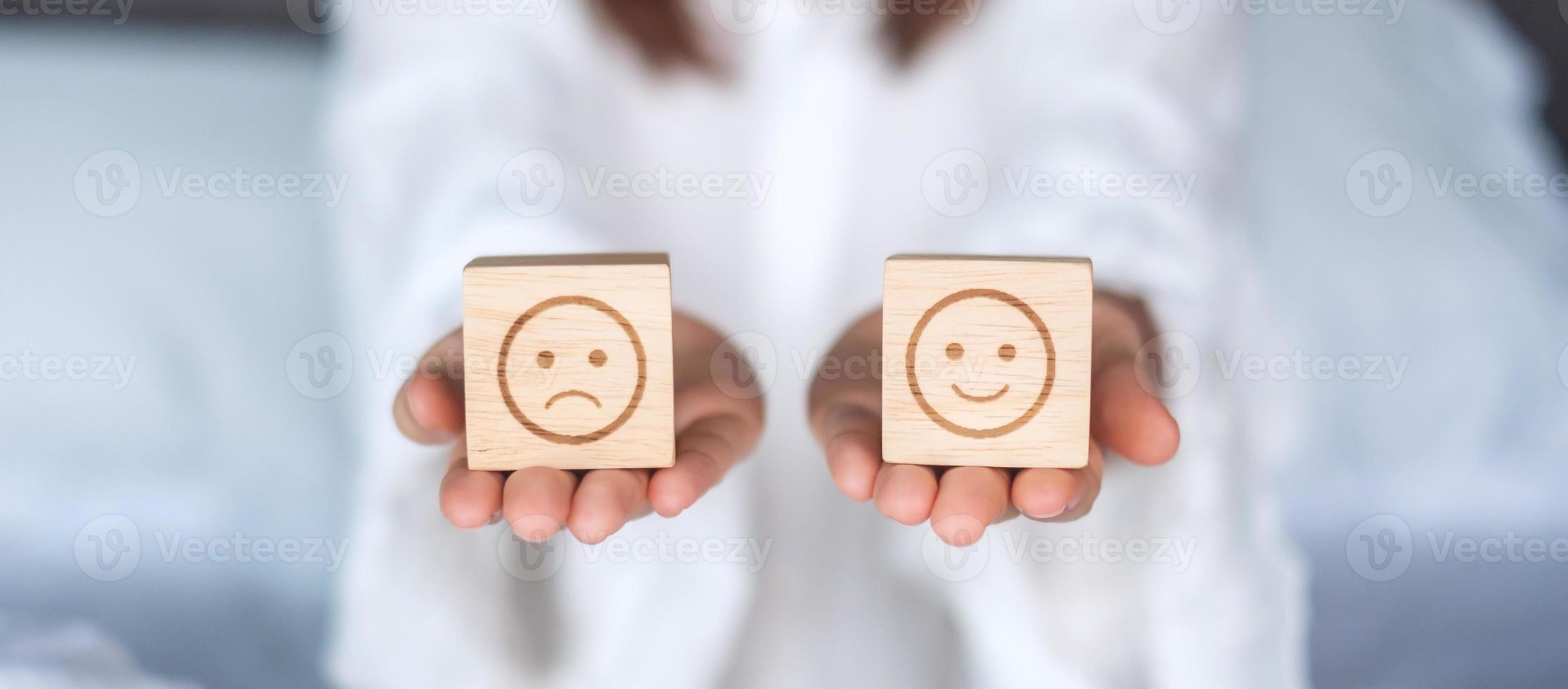 Woman holding smile and angry emotion face block. Customer choose Emoticon for user reviews. Service rating, mental health, positive thinking, satisfaction, evaluation and feedback concept photo