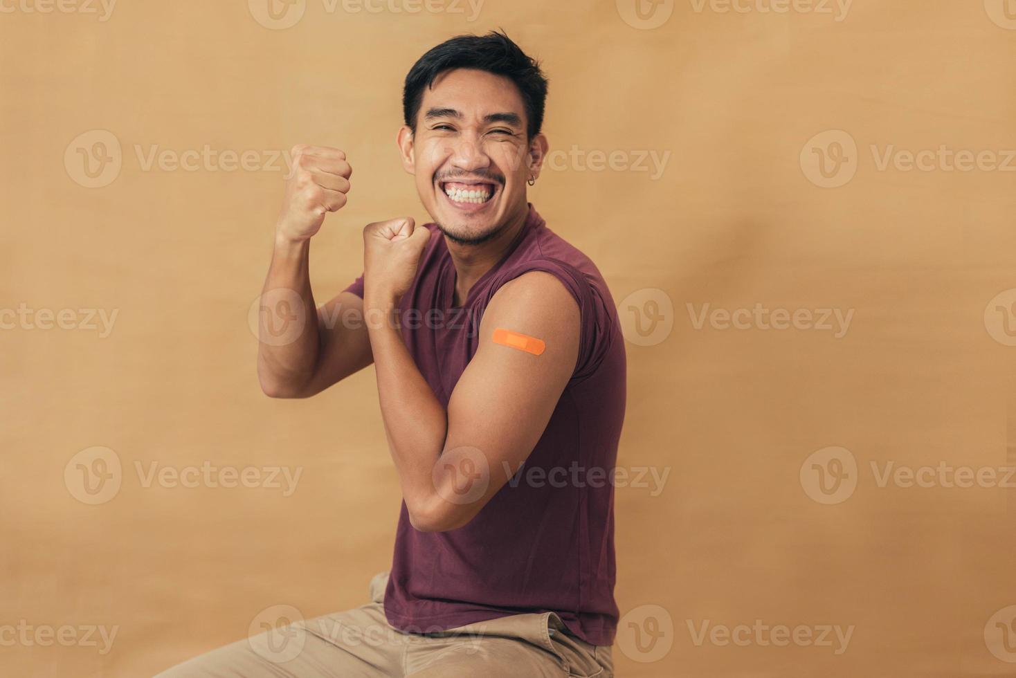 Asian man showing shoulders after getting a vaccine. Happy man showing arm with band-aids on after vaccine injection. photo