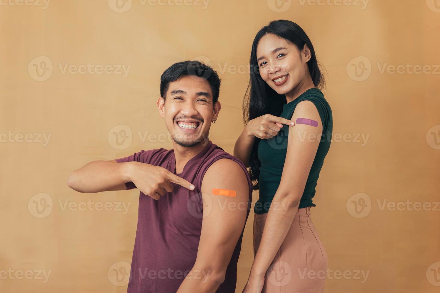 Asian man and woman showing shoulders after getting a vaccine. Happy couple showing arm with band-aids on after vaccine injection. photo