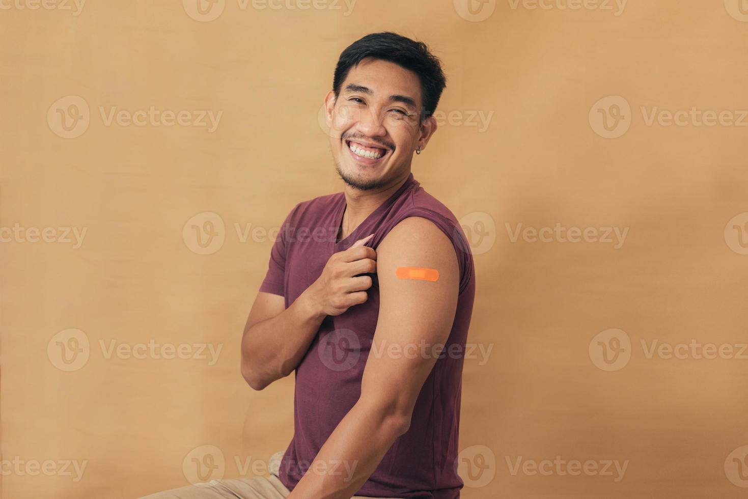 Asian man showing shoulders after getting a vaccine. Happy man showing arm with band-aids on after vaccine injection. photo