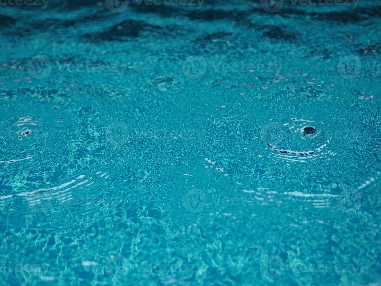 gotas de lluvia que caen agua azul en el fondo de la piscina ondulaciones en la textura de la superficie, resumen de bokeh brillante foto