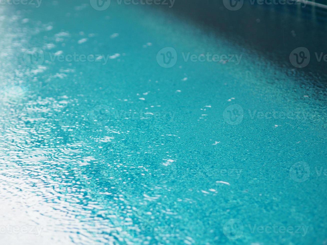 Rain drops falling blue water in pool background ripples on the surface texture, glittering bokeh abstract photo