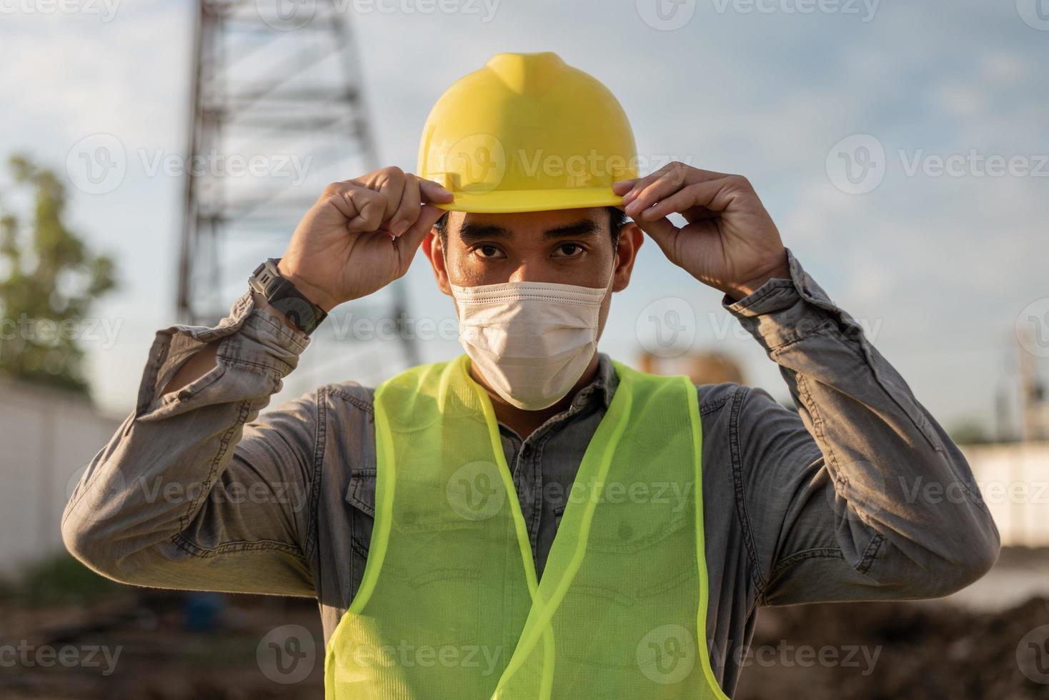 Engineer man wearing face mask and working in building site. Young worker man working in construction site. photo