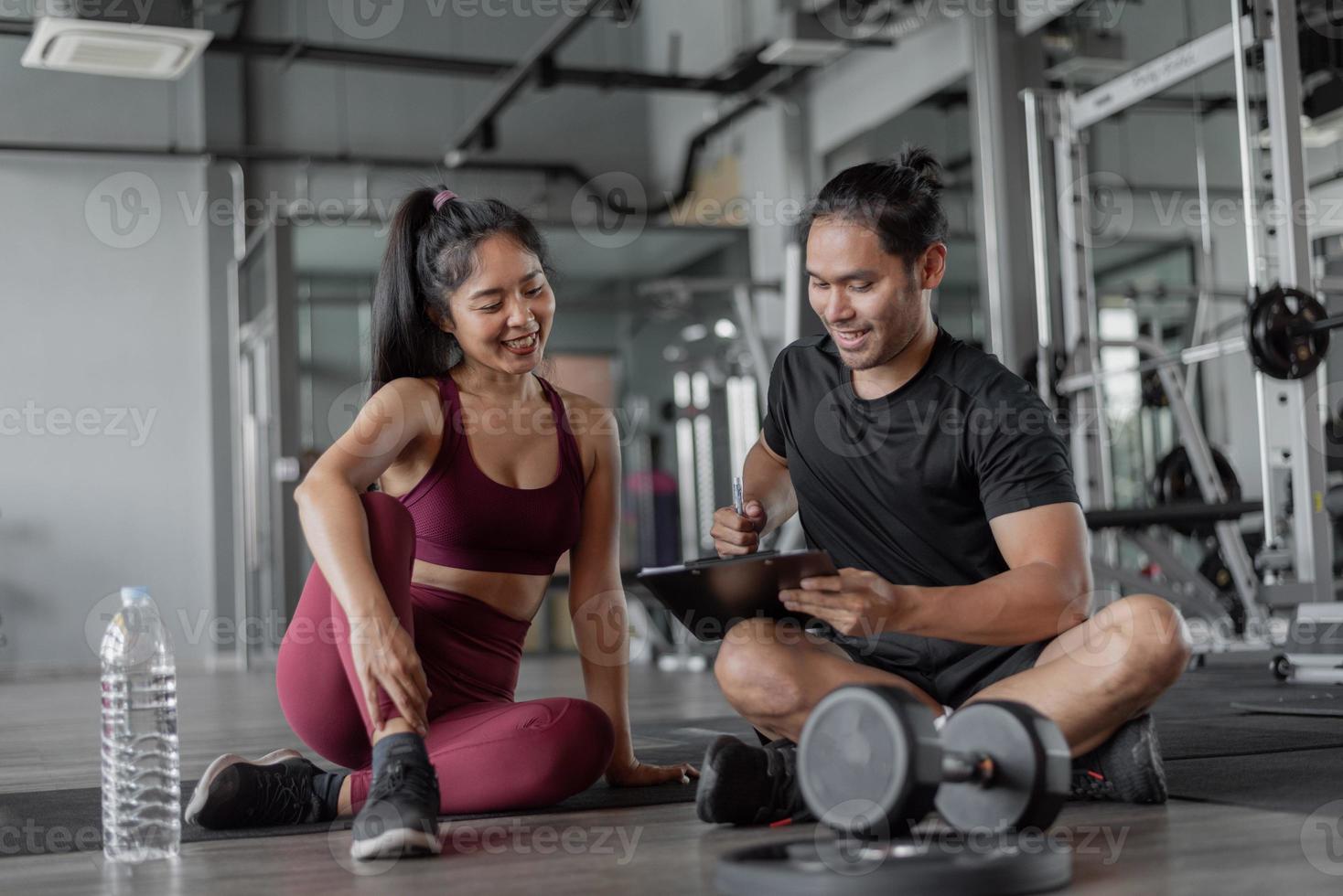 Asian woman exercise with personal trainer in gym. Personal trainer showing and talking about exercise plan with  healthy woman. photo