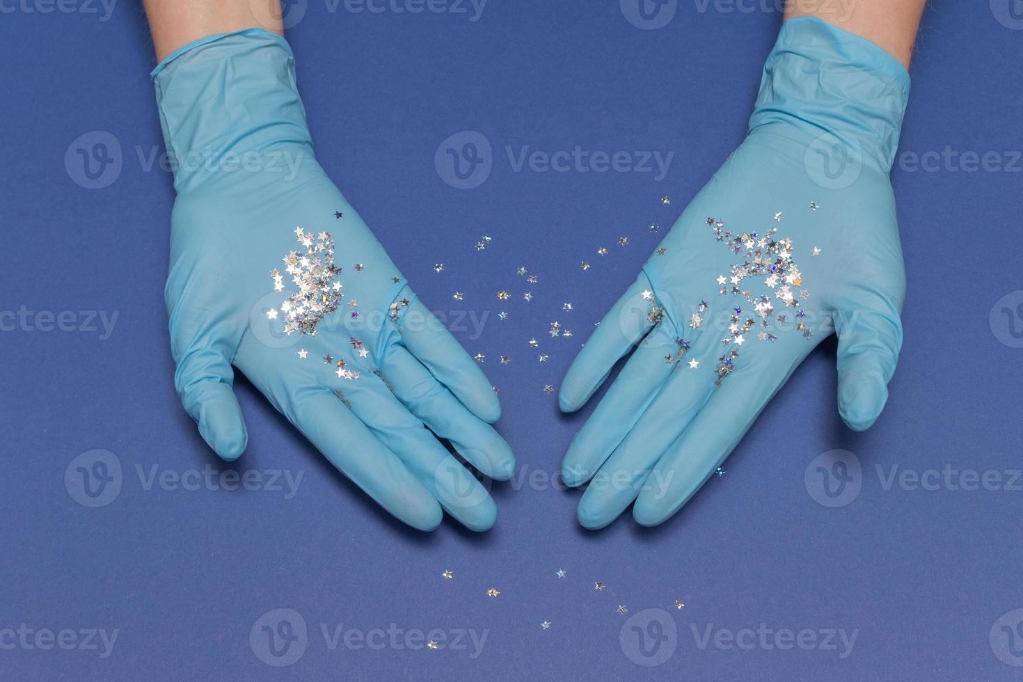 Hands in medical gloves on blue background. Glitter little stars in hands. Christmas and New Year card concept. Top view photo, copy space. photo
