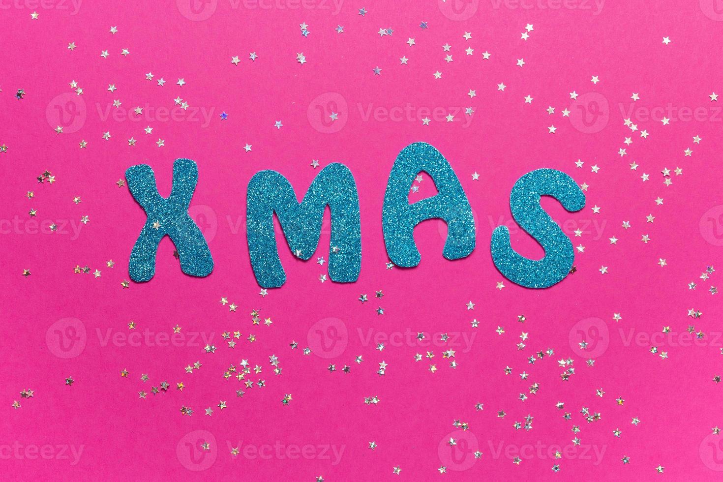 Word Xmas on pink background with glittered little stars. Christmas inscription with space for text writing, greeting. Concept banner for Christmas card, advertising. Top view. High quality photo