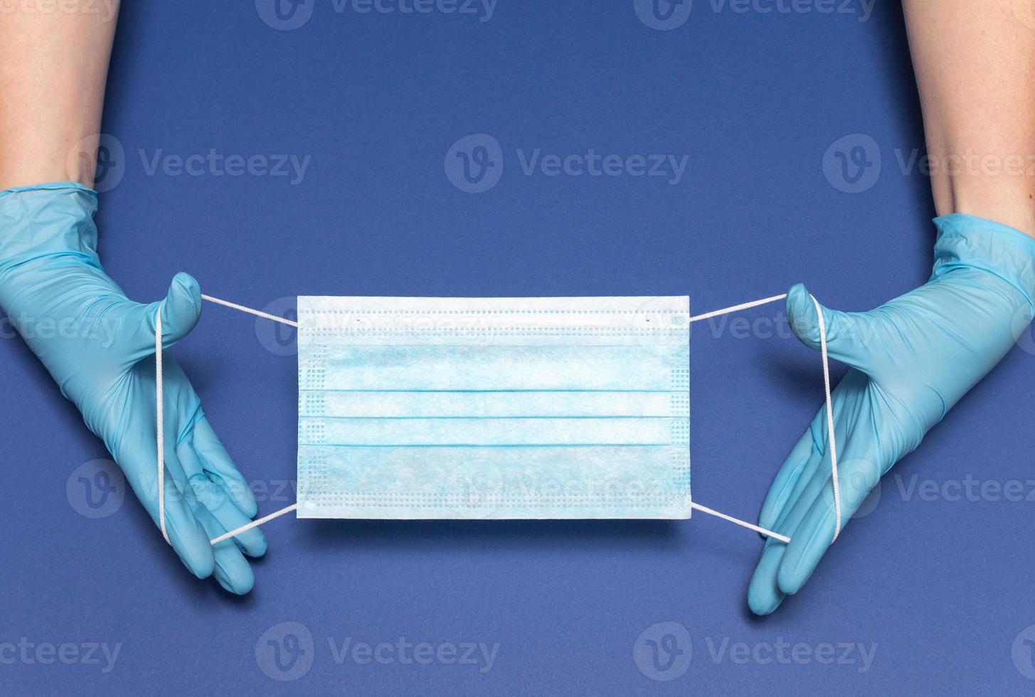 Hands in blue medical gloves is holding face mask on blue background. Protective respiratory medical mask against spreading virus. Close up, copy space, top view, flat lay. High quality photo