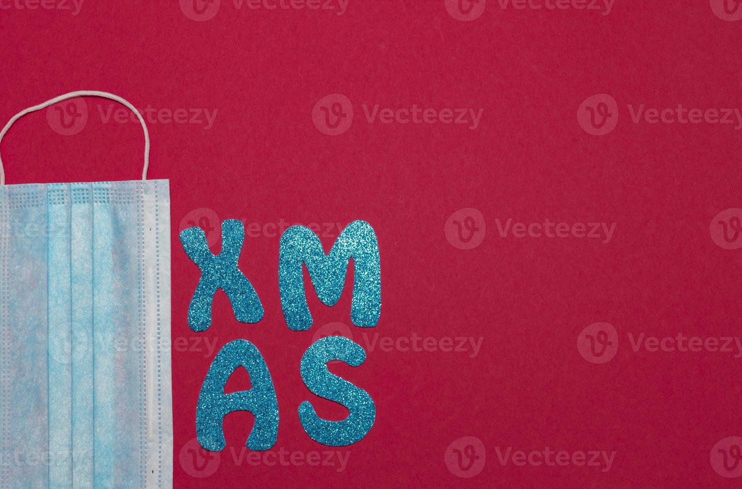 Medical protective mask on red background. Inscription Xmas. Christmas and New Year card, banner, advertising concept. Top view photo, minimalism, copy space. Medical flatly. photo